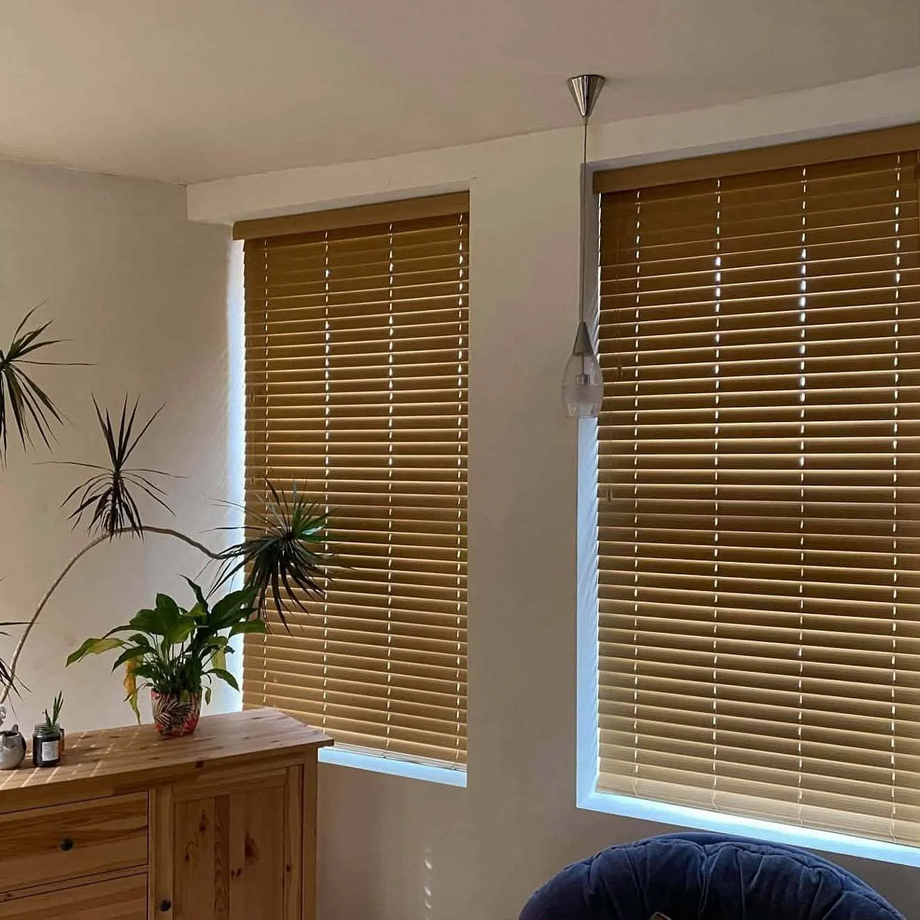 Living room with three large window blinds, a wooden sideboard, a potted plant, and a hanging light fixture.