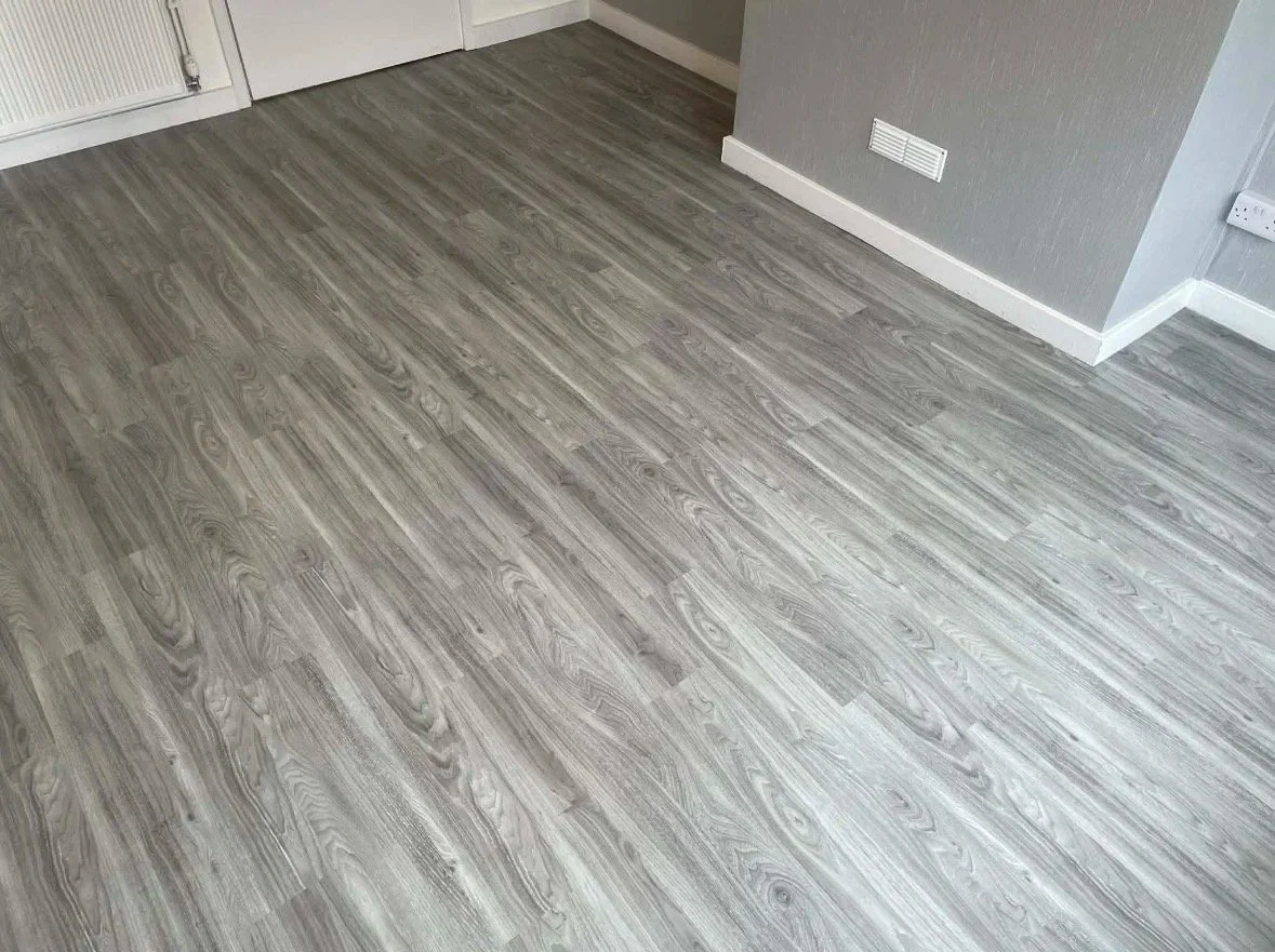 Room with gray wood laminate flooring, white baseboards, a gray wall, and wall vents.