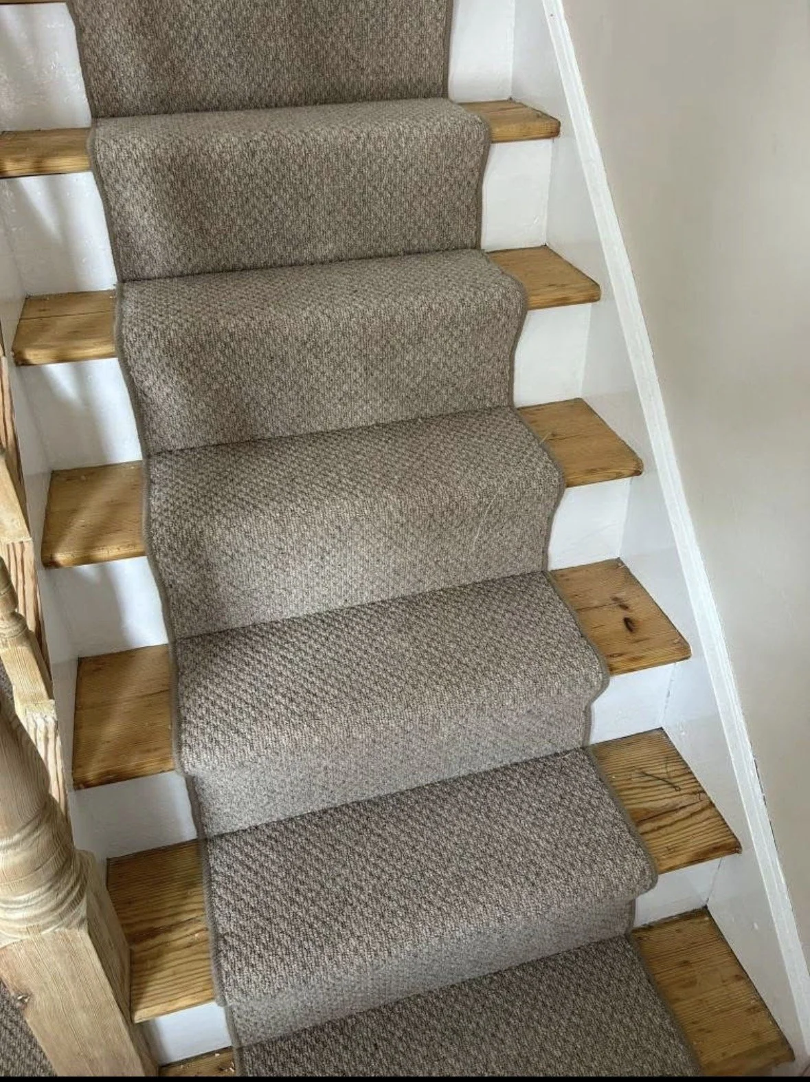 Carpeted staircase with beige carpet and wooden treads, white risers, and white wall on the right side.