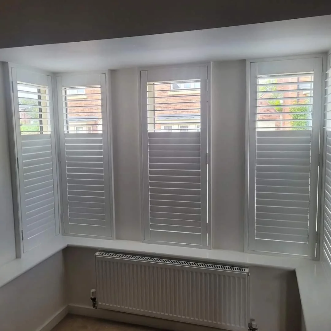 Four windows with white plantation shutters in a room, with a white radiator below.