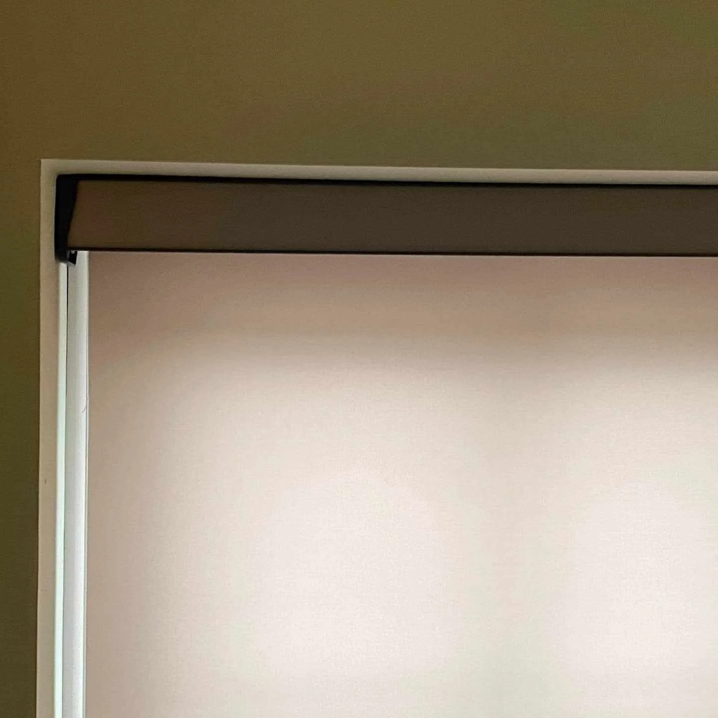 Partially open window shade over a beige wall or window with visible trim.