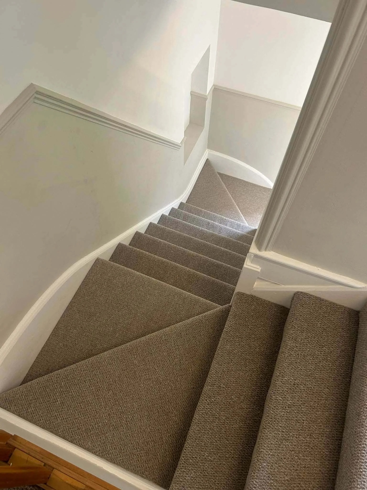 A staircase with brown carpeted steps, white walls, and a curved wall at the bottom of the stairs.