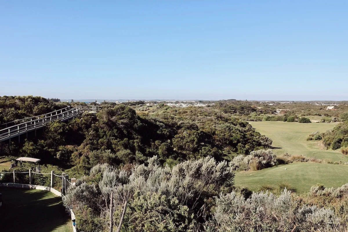 A scenic view of a golf course with green fairways, surrounded by trees and shrubs, under a clear blue sky.