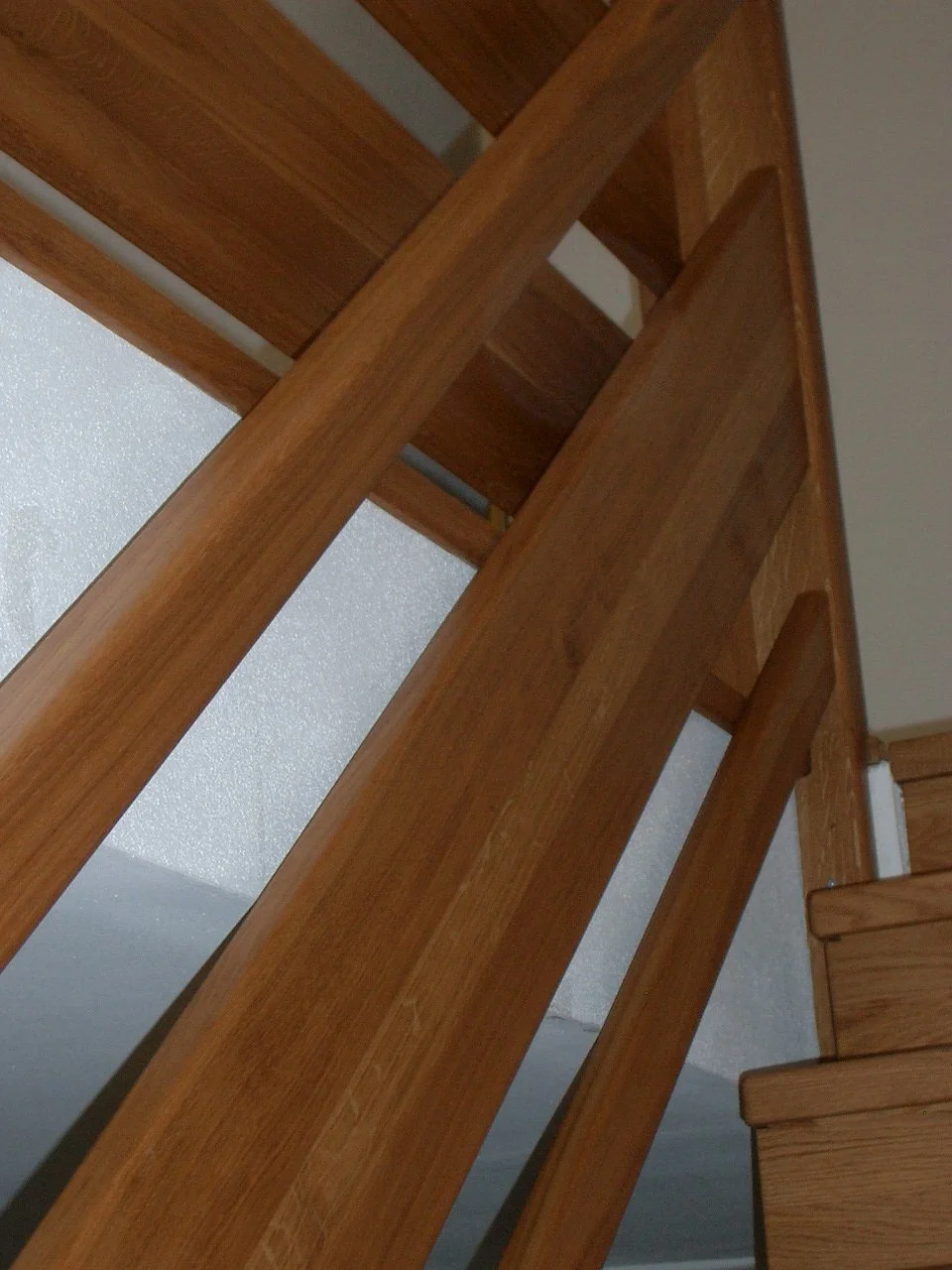 Close-up of a wooden staircase and handrail from below, with ceiling and wall in the background.