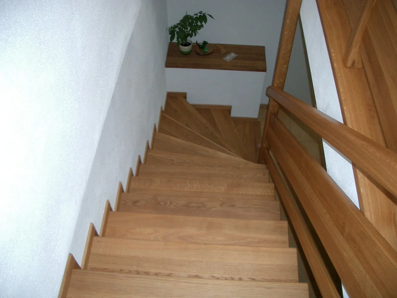 View of a wooden staircase looking downward with a small landing and a potted plant on a ledge at the bottom.