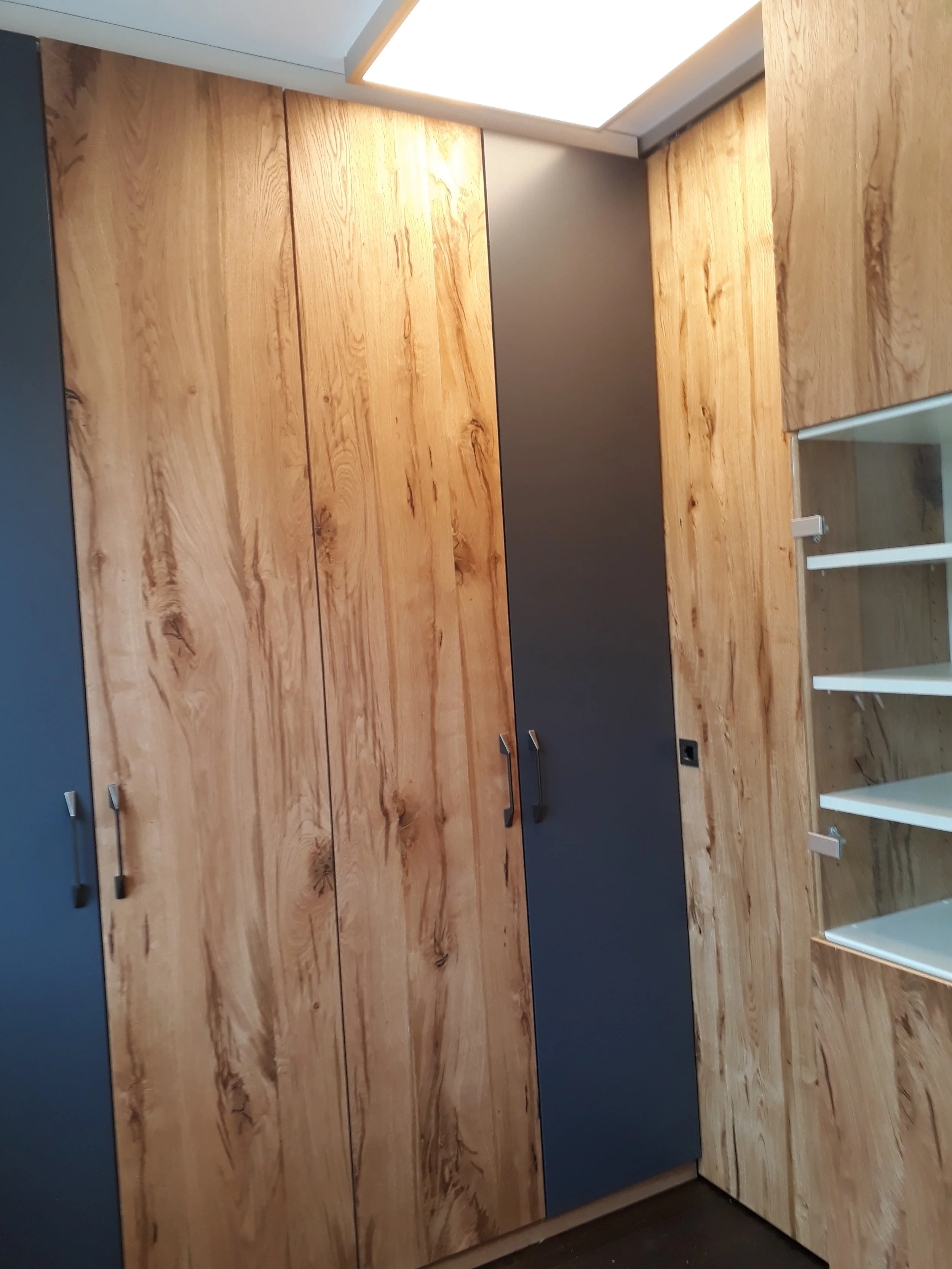 Wooden cabinets with black handles in a modern kitchen, with a portion of white shelving visible in the bottom right corner.