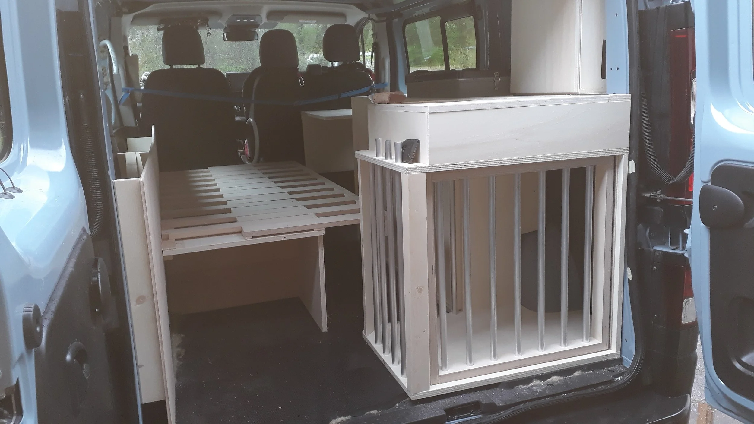 Interior of a van with custom wooden furniture, including storage cabinets and a slatted platform, possibly for camping or traveling.