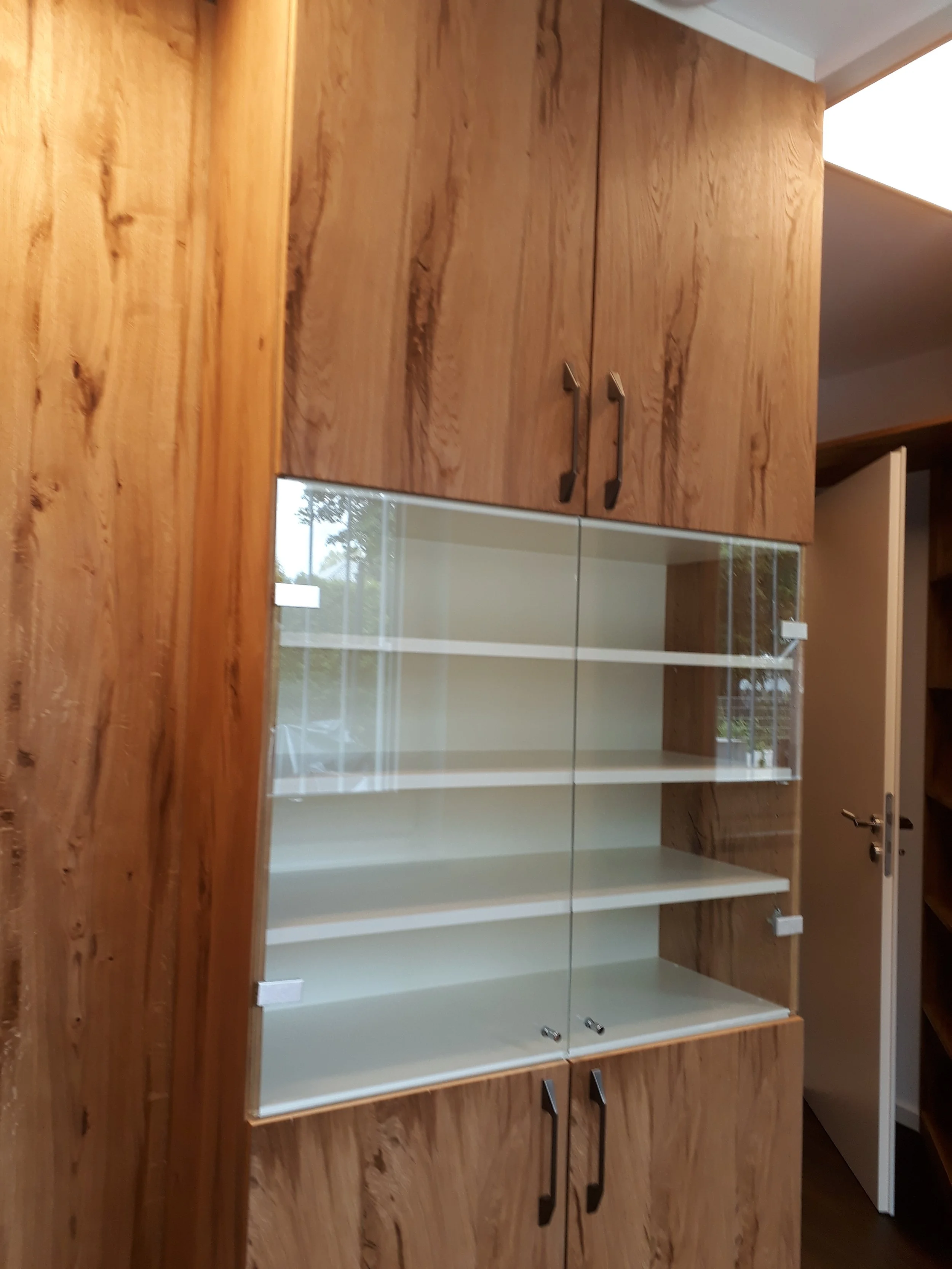 Wooden kitchen cabinets with black handles, some doors are open revealing white shelves inside. The image is upside down.