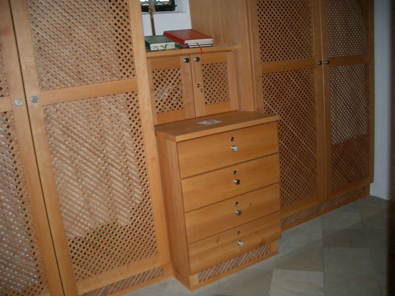Wooden cabinet with sliding lattice doors and a small set of drawers, placed on a tiled floor.