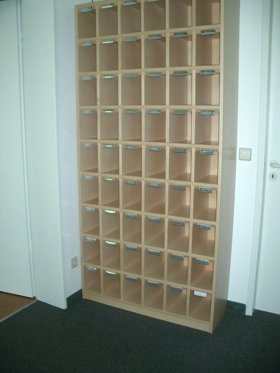 Empty wooden cubby shelf with multiple small compartments, each with a metal label holder inside.