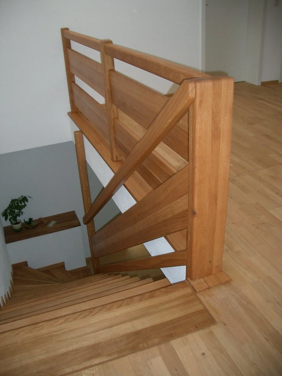 Wooden staircase viewed from the top, leading down to a hallway with a potted plant on a small table.