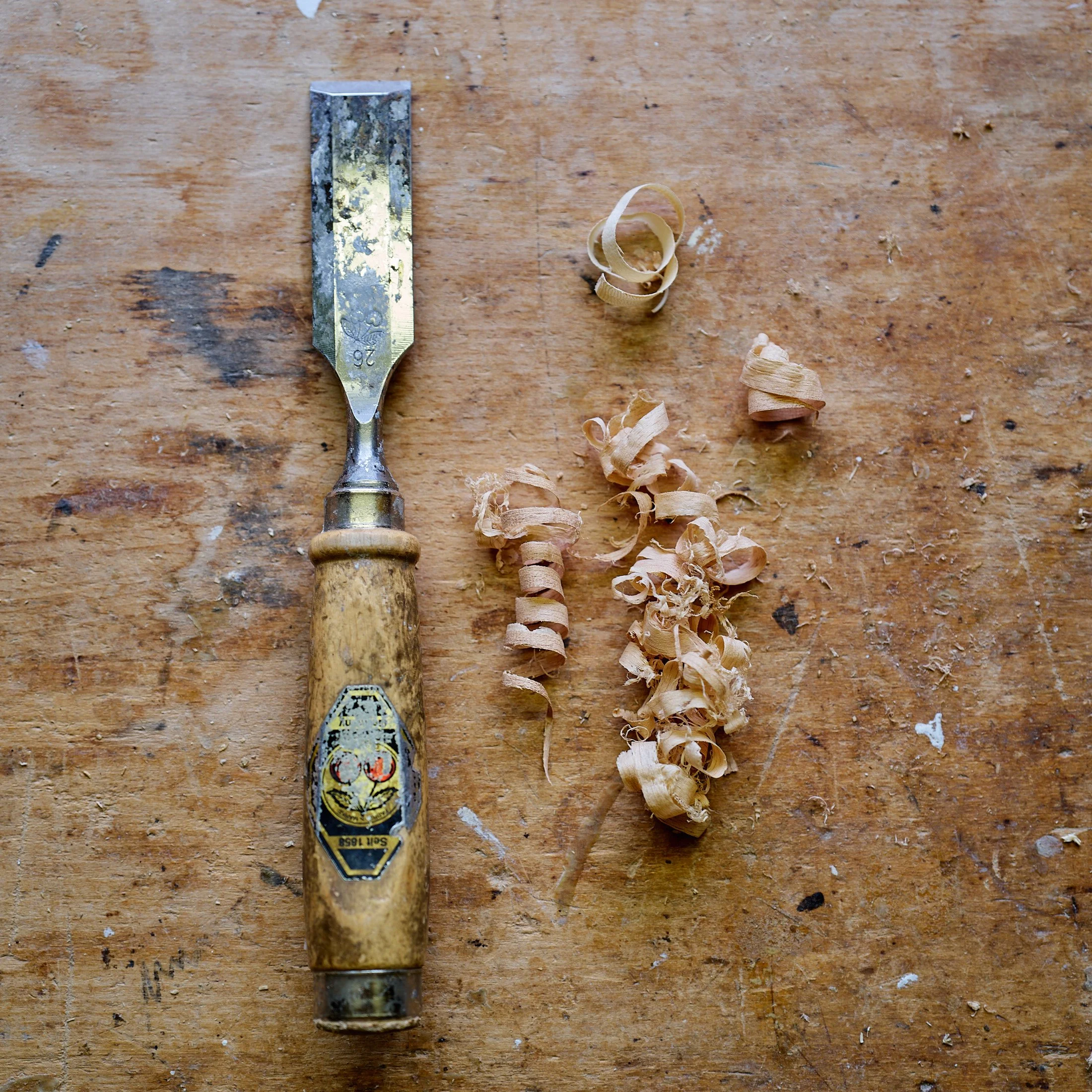 Ein Stemmeisen mit gelbem Griff, einer kleinen Metallspitze und Holzspänen auf einer hölzernen Arbeitsfläche.