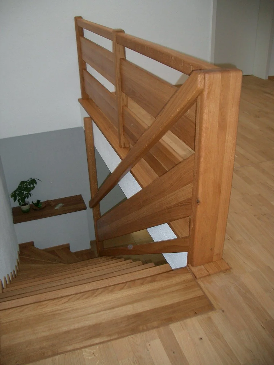 Wooden staircase with a newel post, handrails, and horizontal slats, leading down to a lower floor.