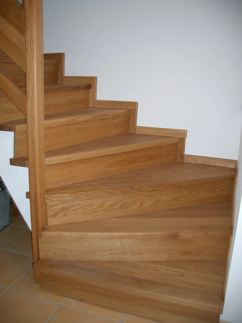 A wooden staircase with four steps leading to an upper level, with white walls and tiled flooring.