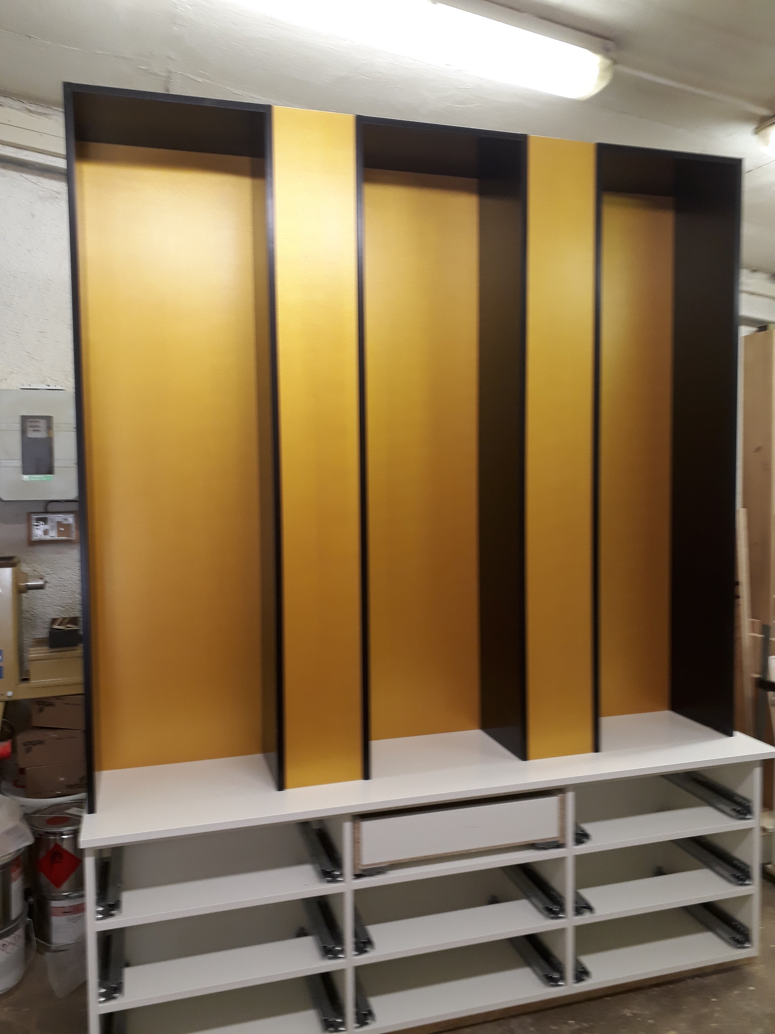 Empty black and yellow bookcase or shelving unit with no items on it, placed in an industrial or storage room with fluorescent lighting.