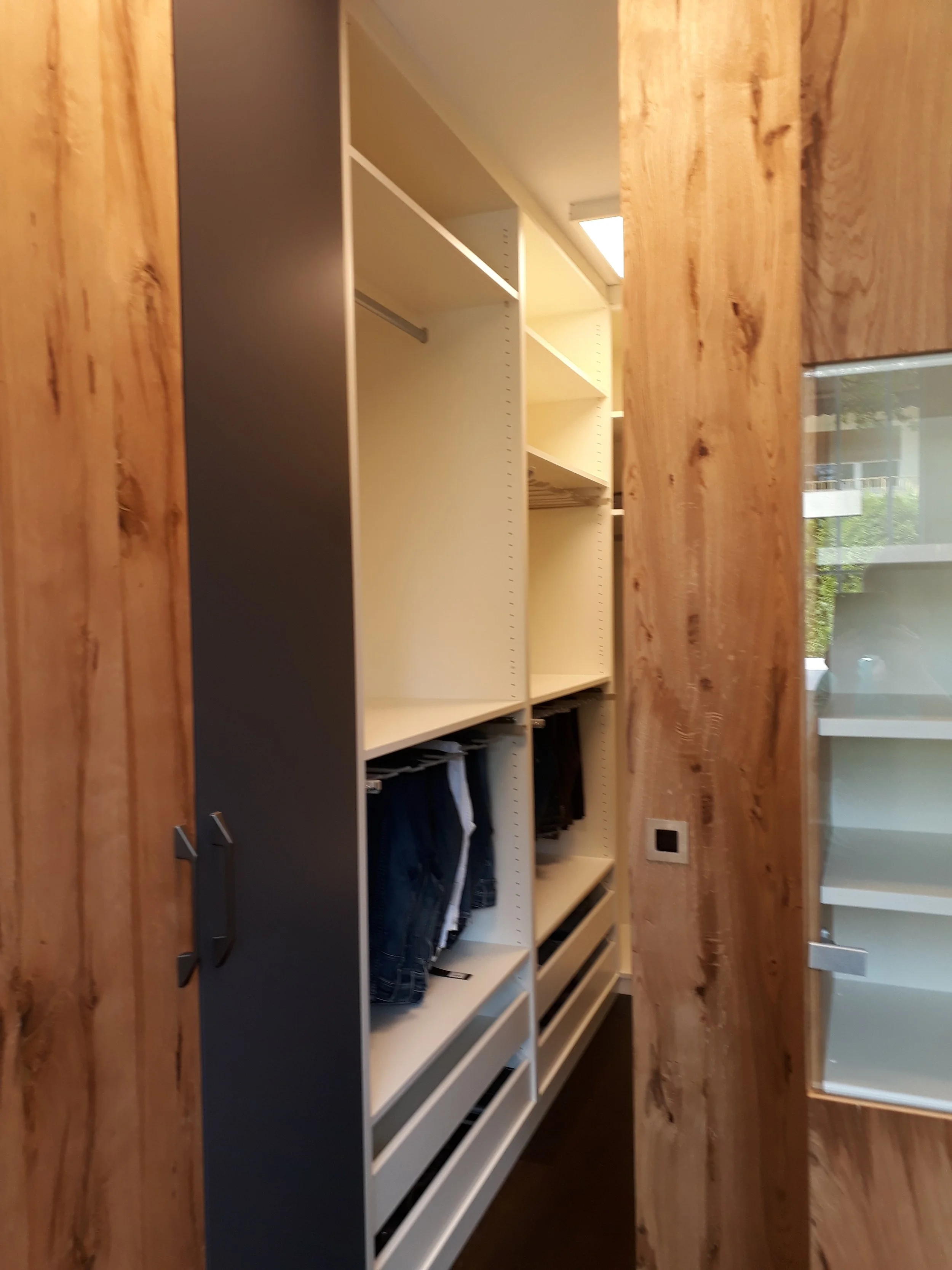 Empty white shelving unit with black bottom drawers placed on a wooden floor in front of a window.