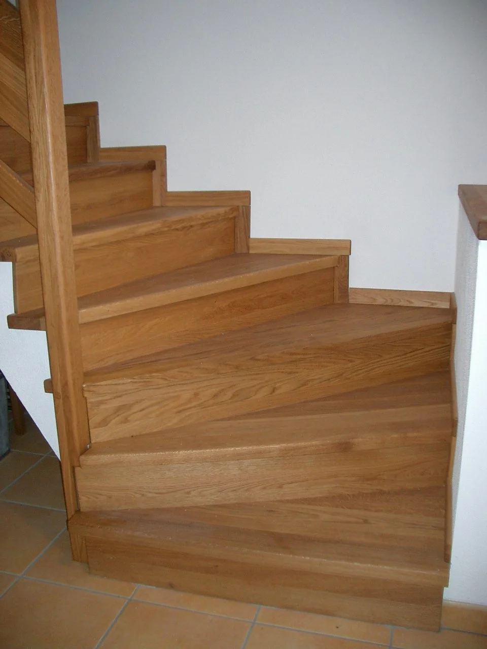 Interior view of a wooden staircase with curved steps installed beside a white wall.