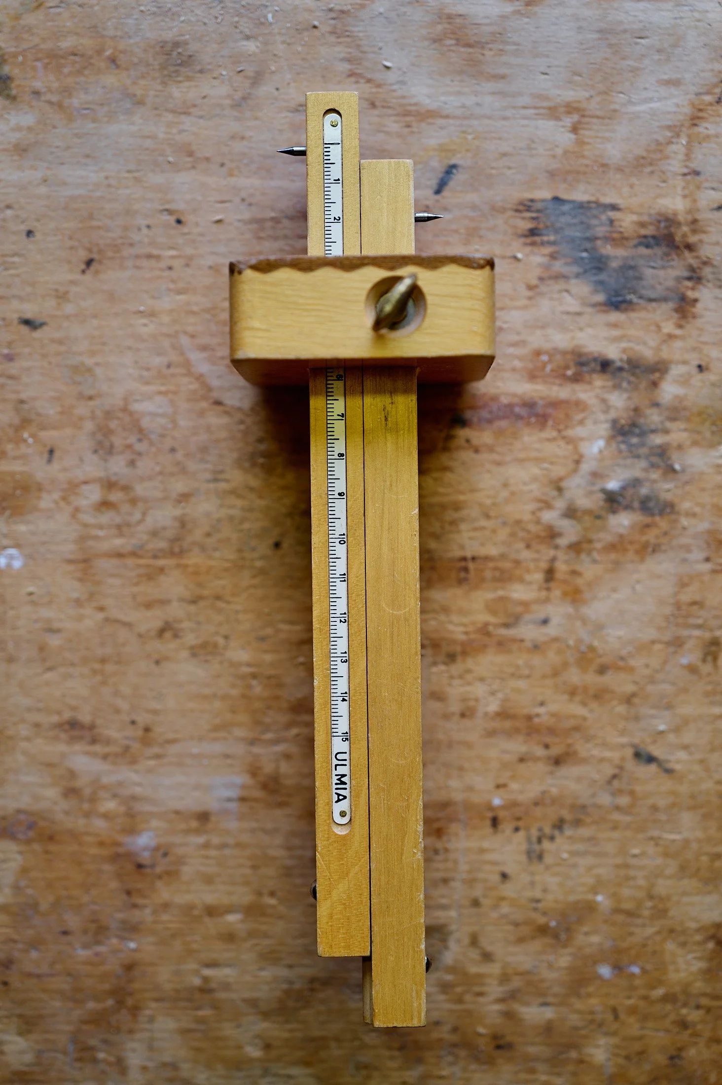 A wooden measuring tool with metal spikes and a ruler, resting on a wooden surface.