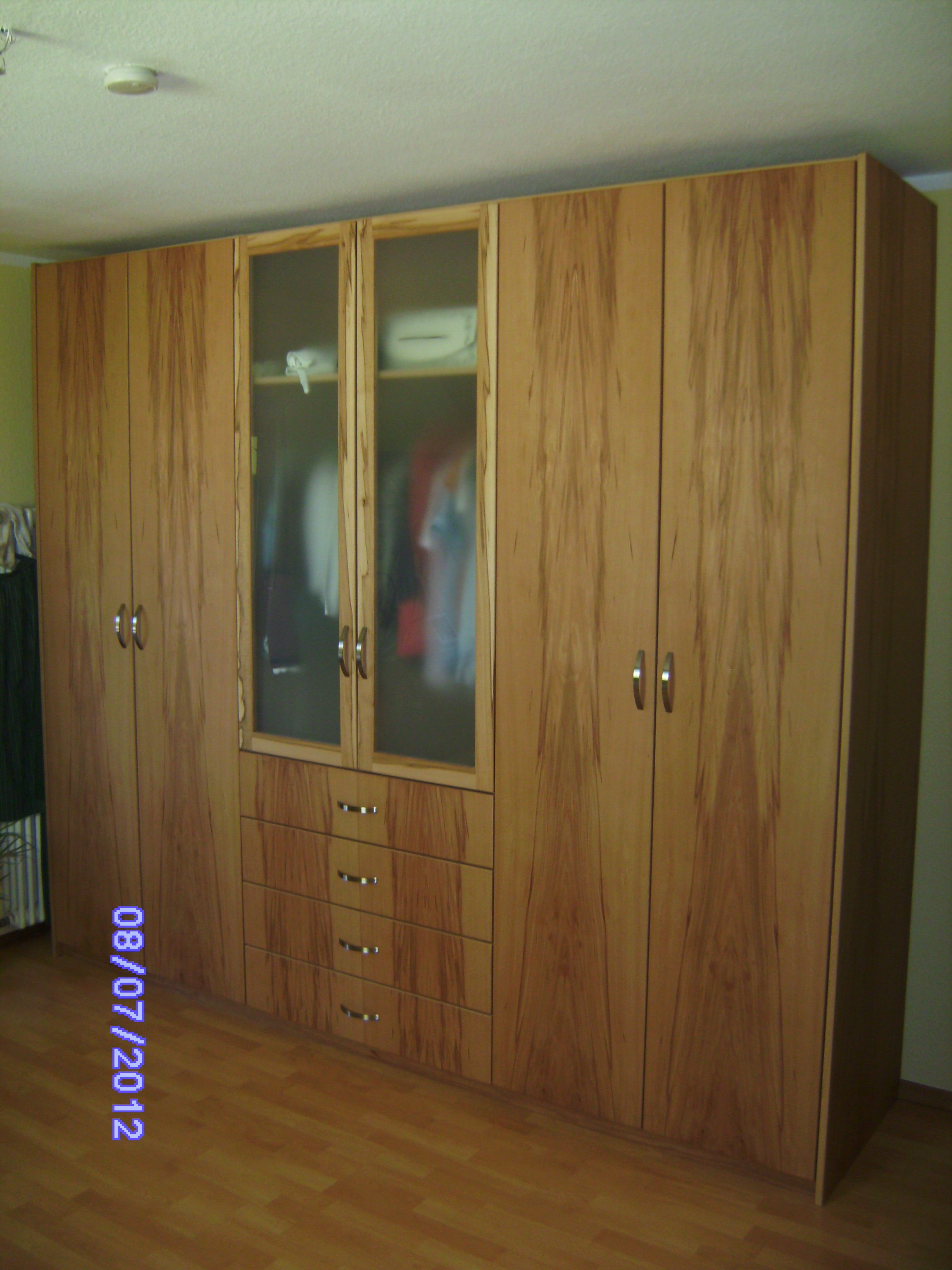 A wooden corner wardrobe with multiple doors and drawers in a room with wooden floor.