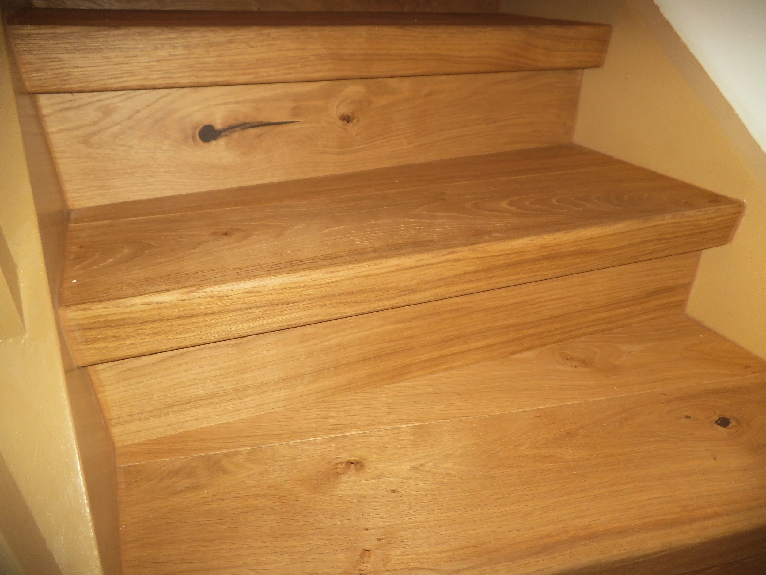 Wooden staircase with four steps, adjacent to a yellow wall and ceiling.