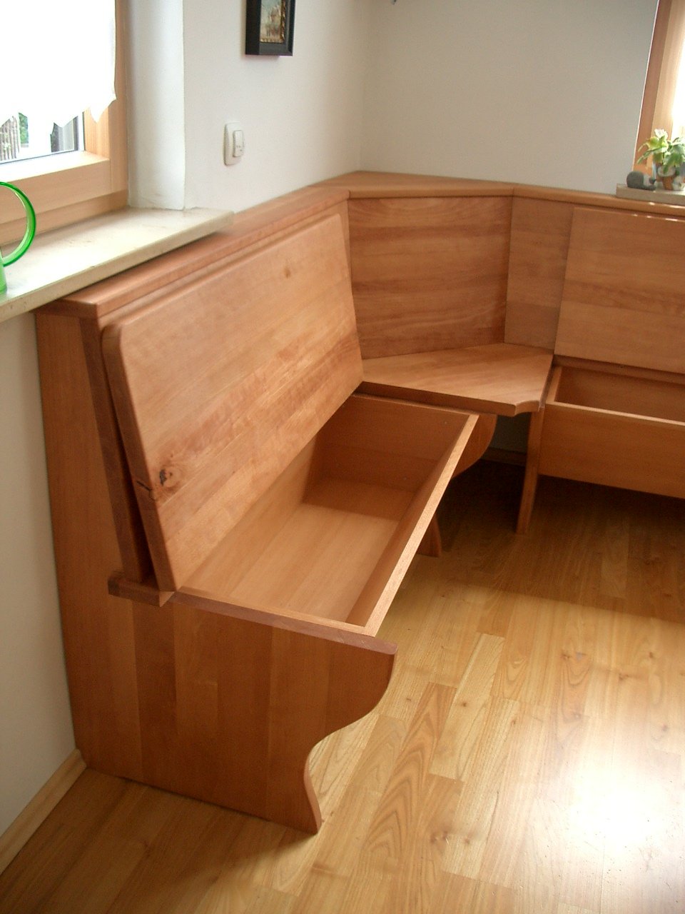 Wooden corner bench with storage compartments in a room with wooden flooring and windows with curtains.