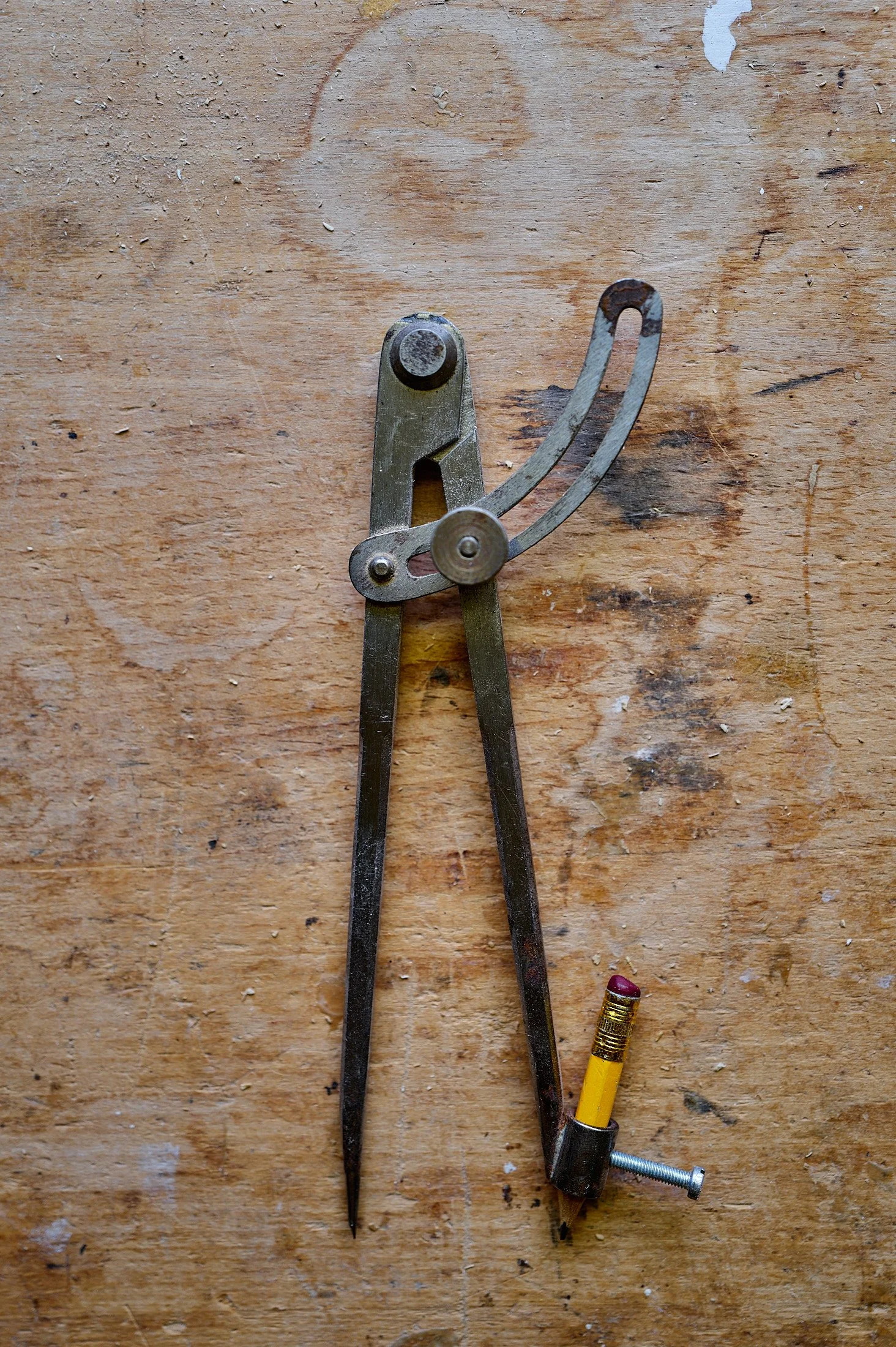 A metal compass, a pencil with an eraser, and a screw on a wooden surface.