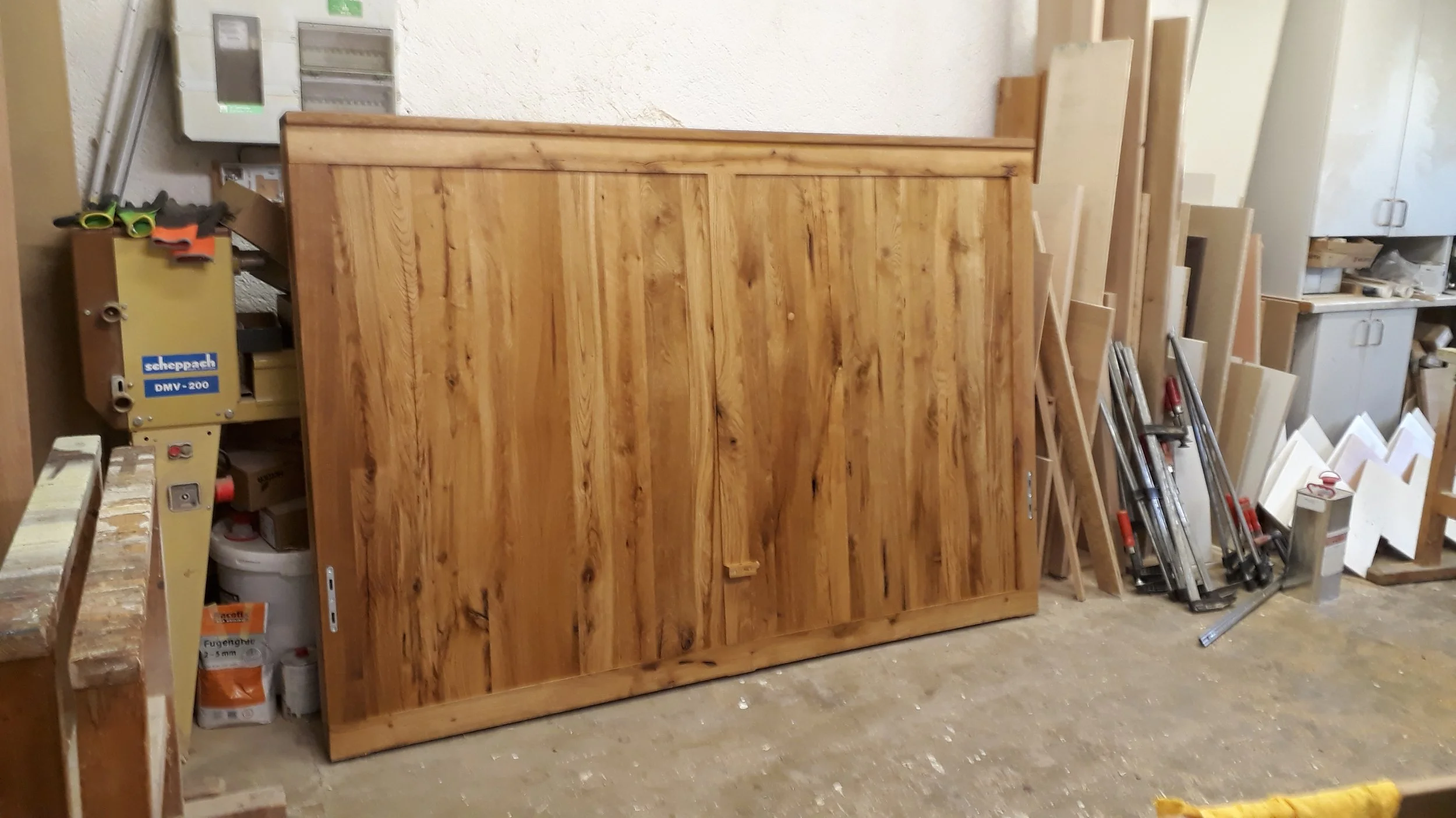 A wooden cabinet or large piece of furniture in a workshop surrounded by tools, wood pieces, and construction materials.