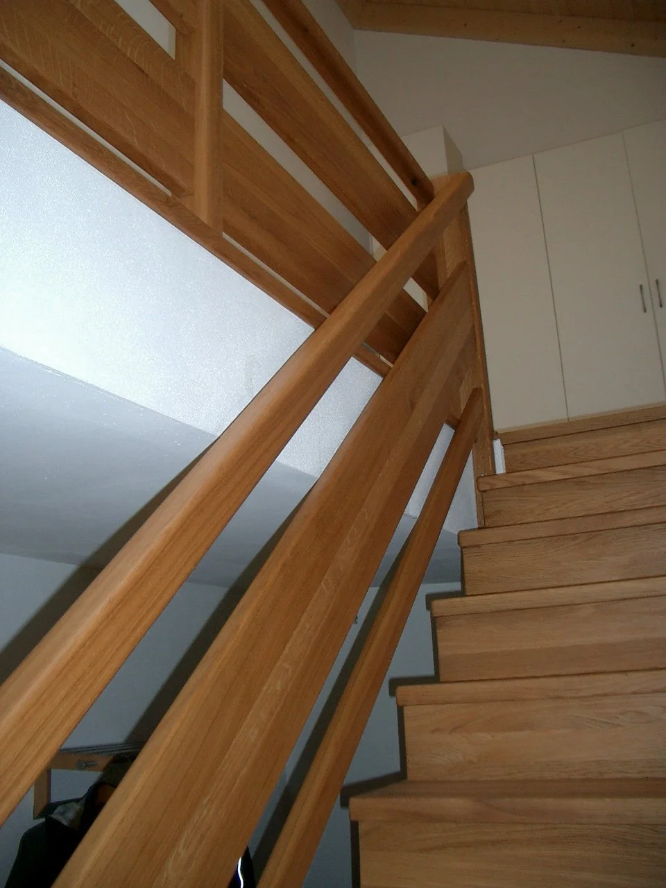 Wooden staircase with a wooden handrail in a house interior.