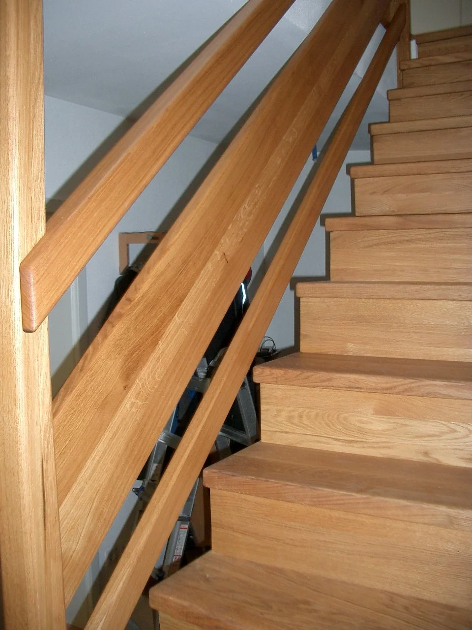 Wooden staircase with a matching handrail and a gray wall in the background.