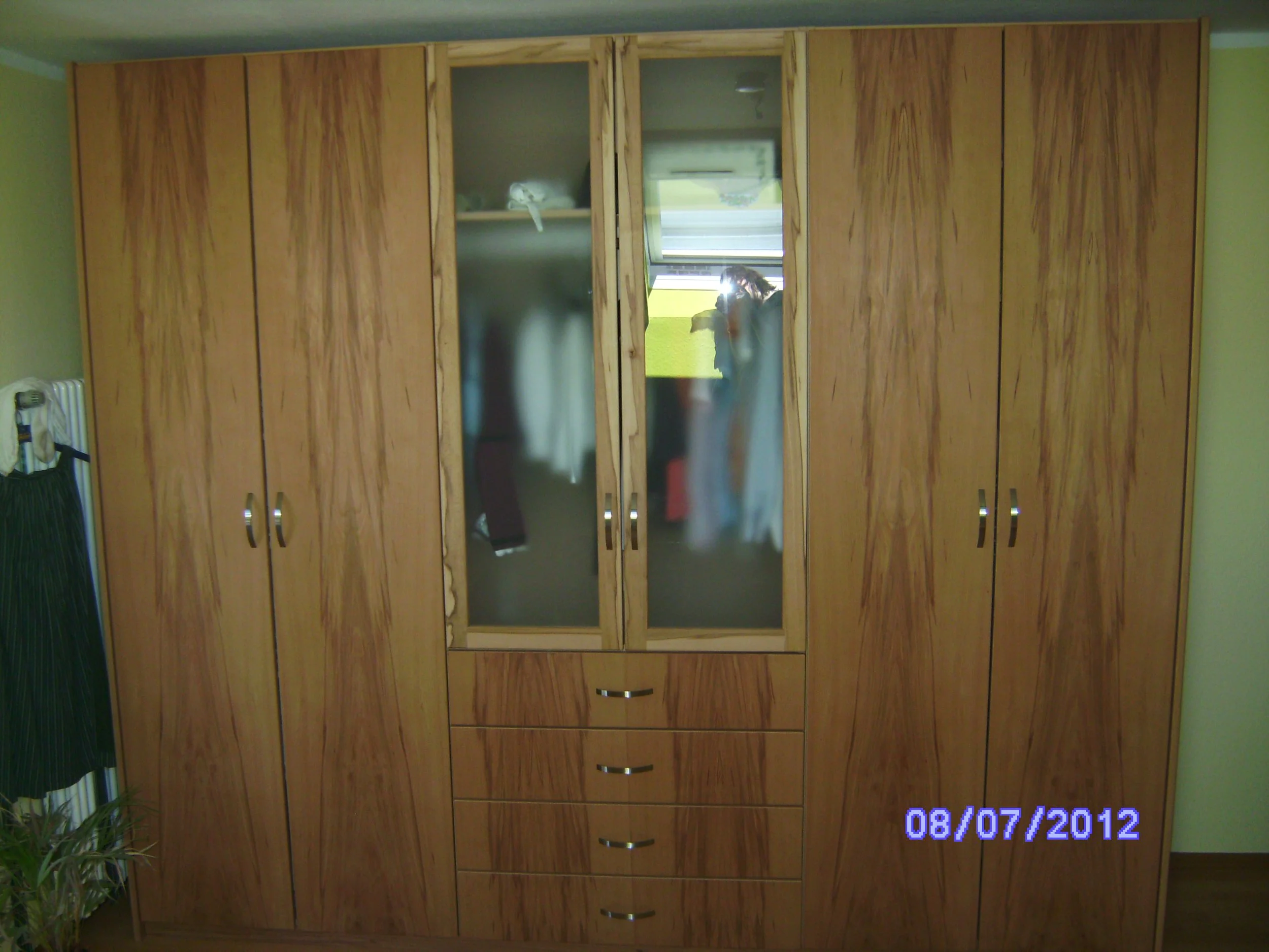 A wooden wardrobe with six doors and three drawers at the bottom, partially mirrored in the middle doors, in a room with a green wall. The bottom right corner displays the date 08/07/2012.