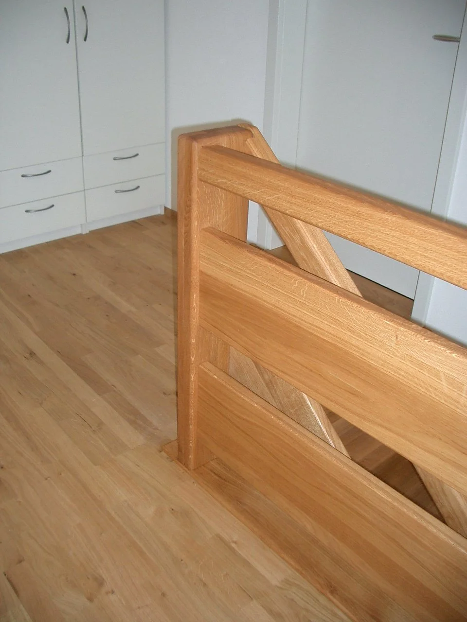 Interior wooden staircase railing with a view of a kitchen with white cabinets and wooden floor.
