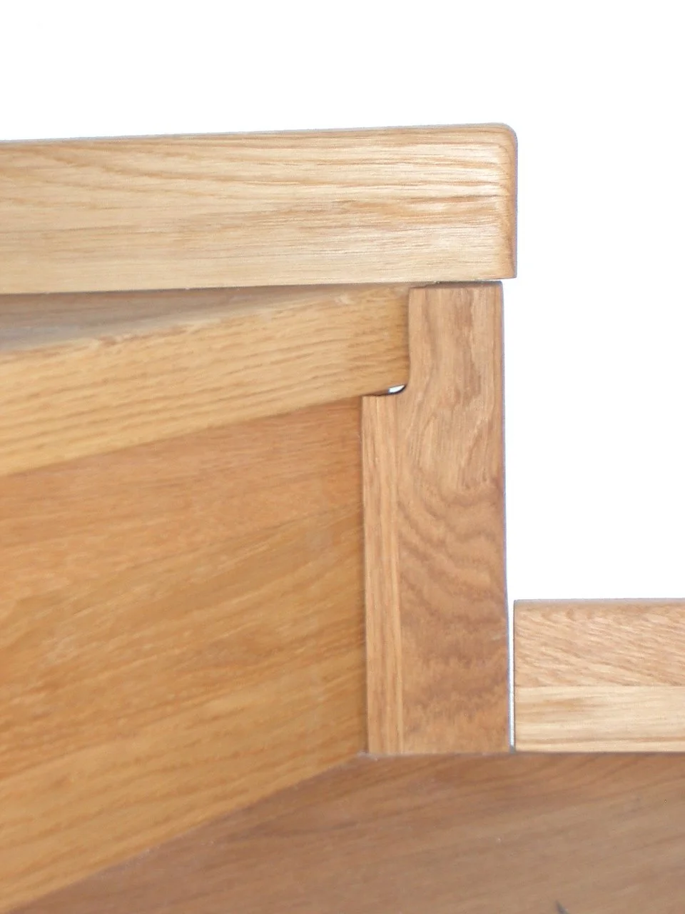 Close-up of a wooden piece of furniture, showing a corner joint with natural wood grain and a light finish.