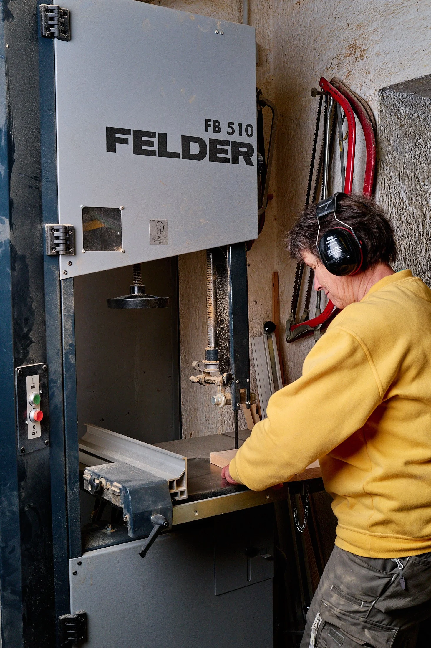 A person wearing a yellow jacket and safety ear protection is working with a woodworking machine in a workshop.