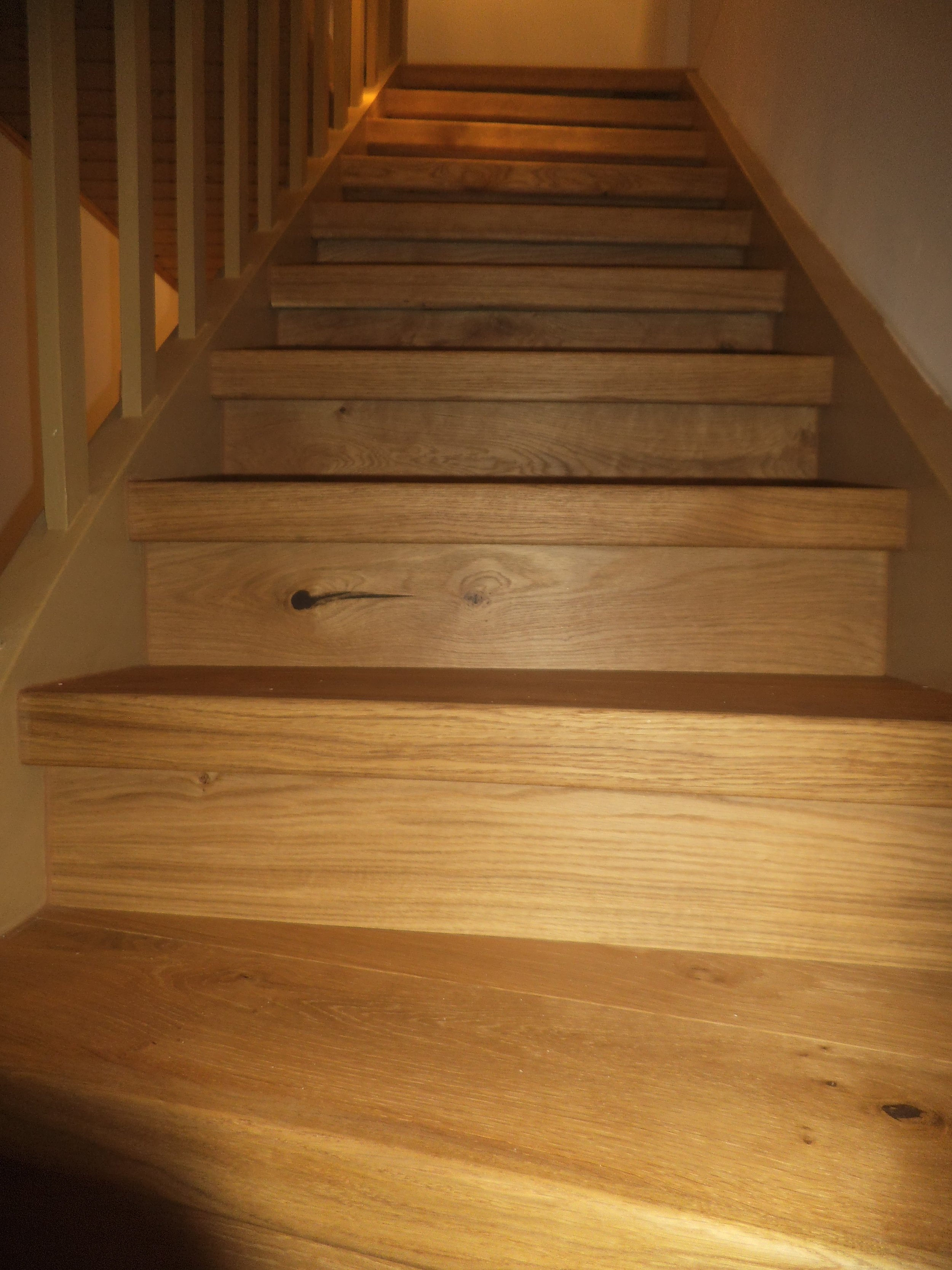 Wooden staircase with horizontal rails and a beige wall on one side.