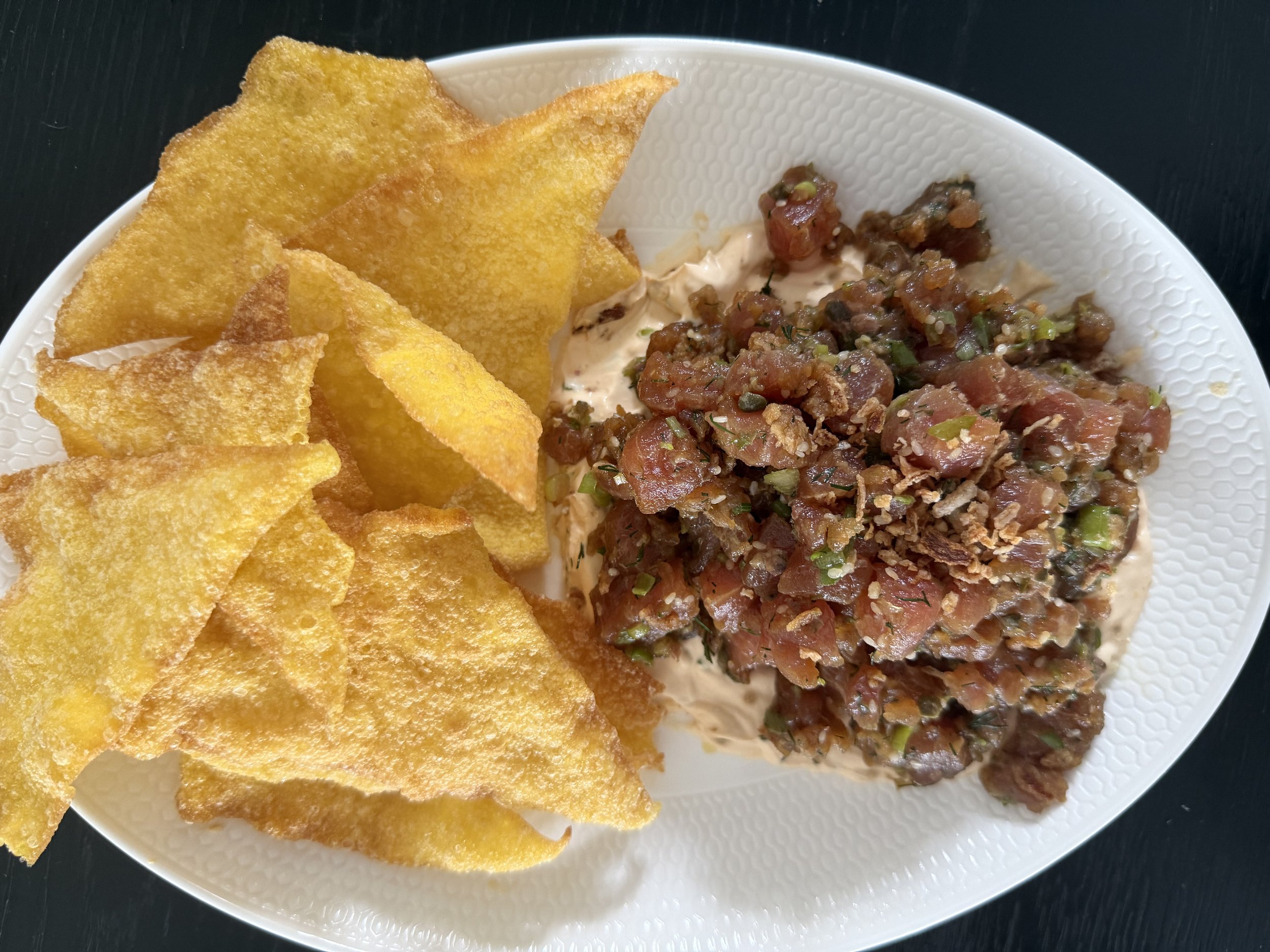 Plate with crispy tortilla chips and a mound of steak tartare topped with green onions or herbs.