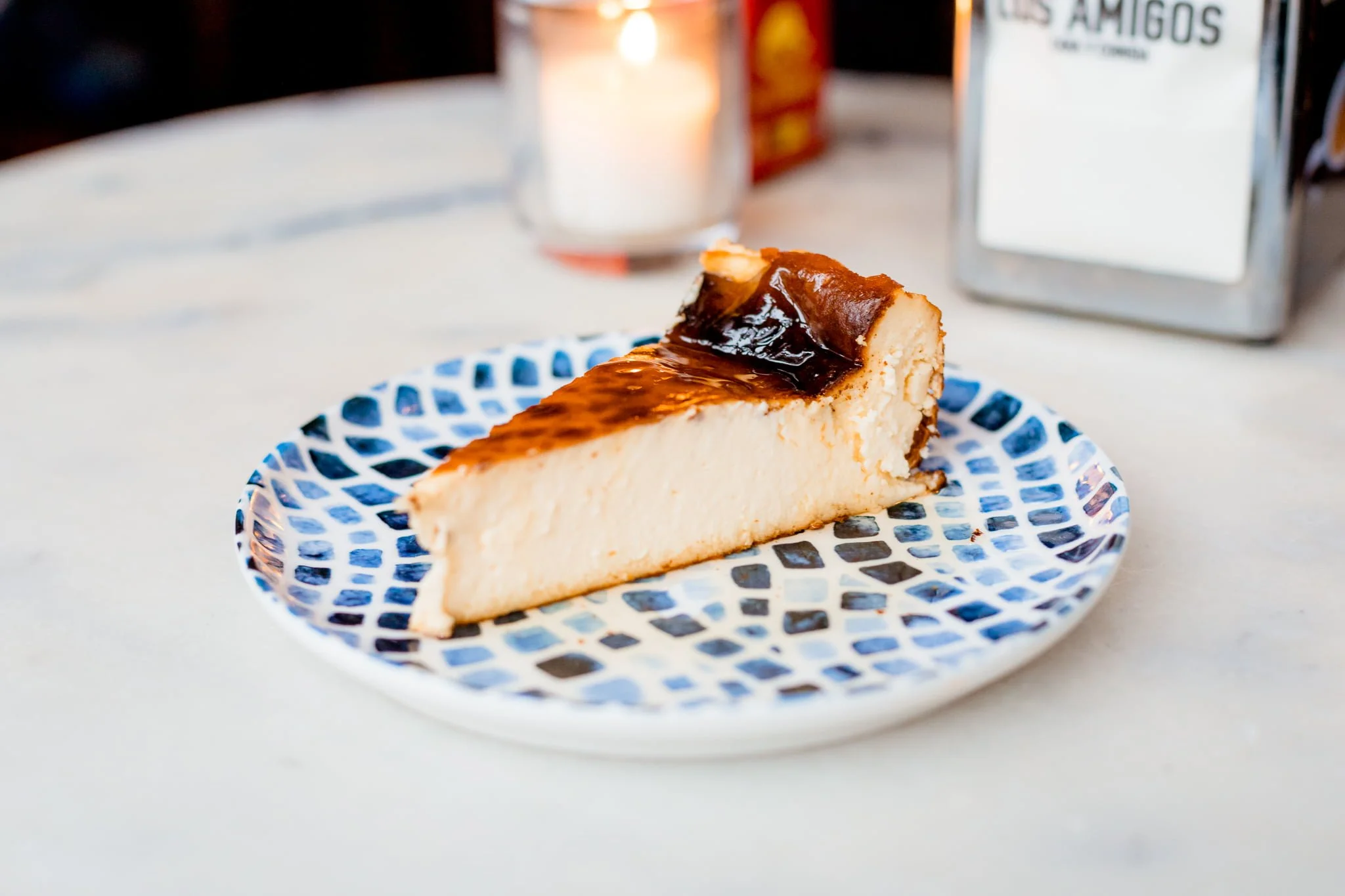 A slice of cheesecake with a caramel glaze on a blue and white patterned plate.