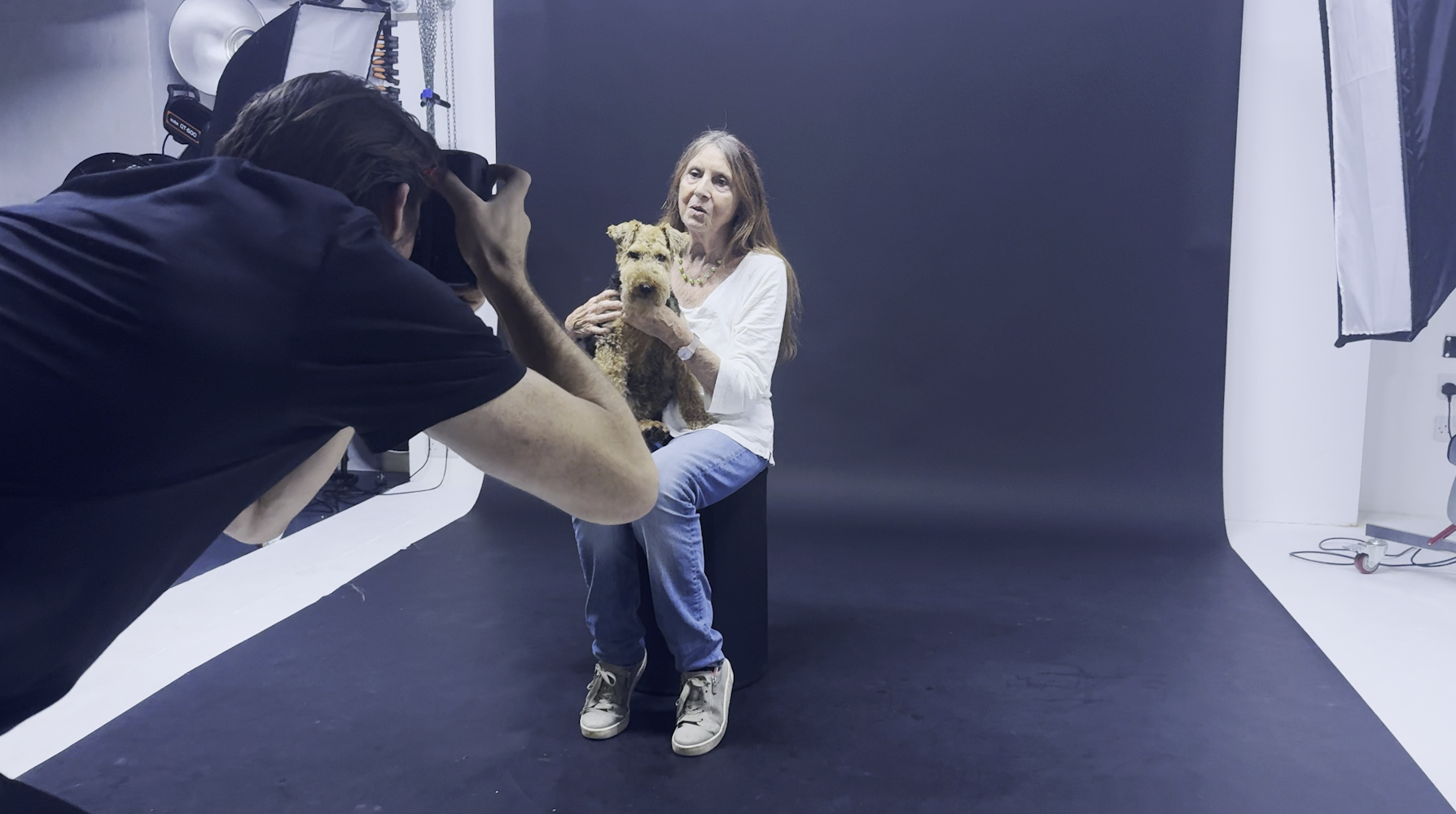 Behind the scenes at the studio, a photographer captures Prue holding Dolly the Welsh Terrier as she sits on a stool against the studio backdrop.