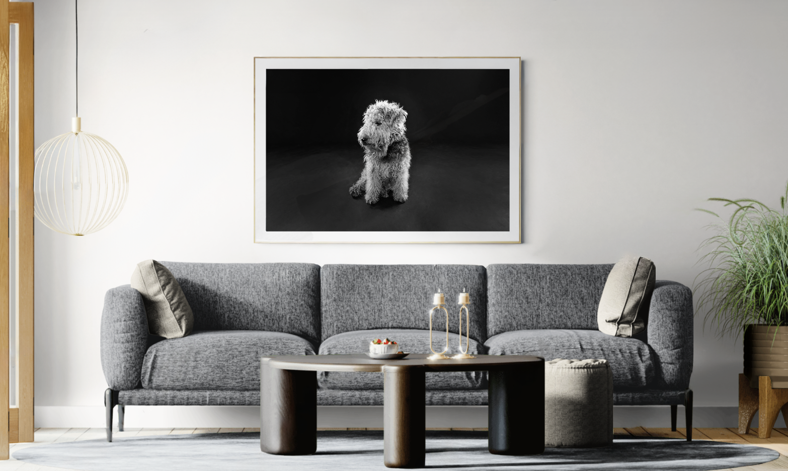 Living room with grey sofa, black and white dog portrait on wall, round lamp, coffee table with bowls and bottles, and indoor plants.