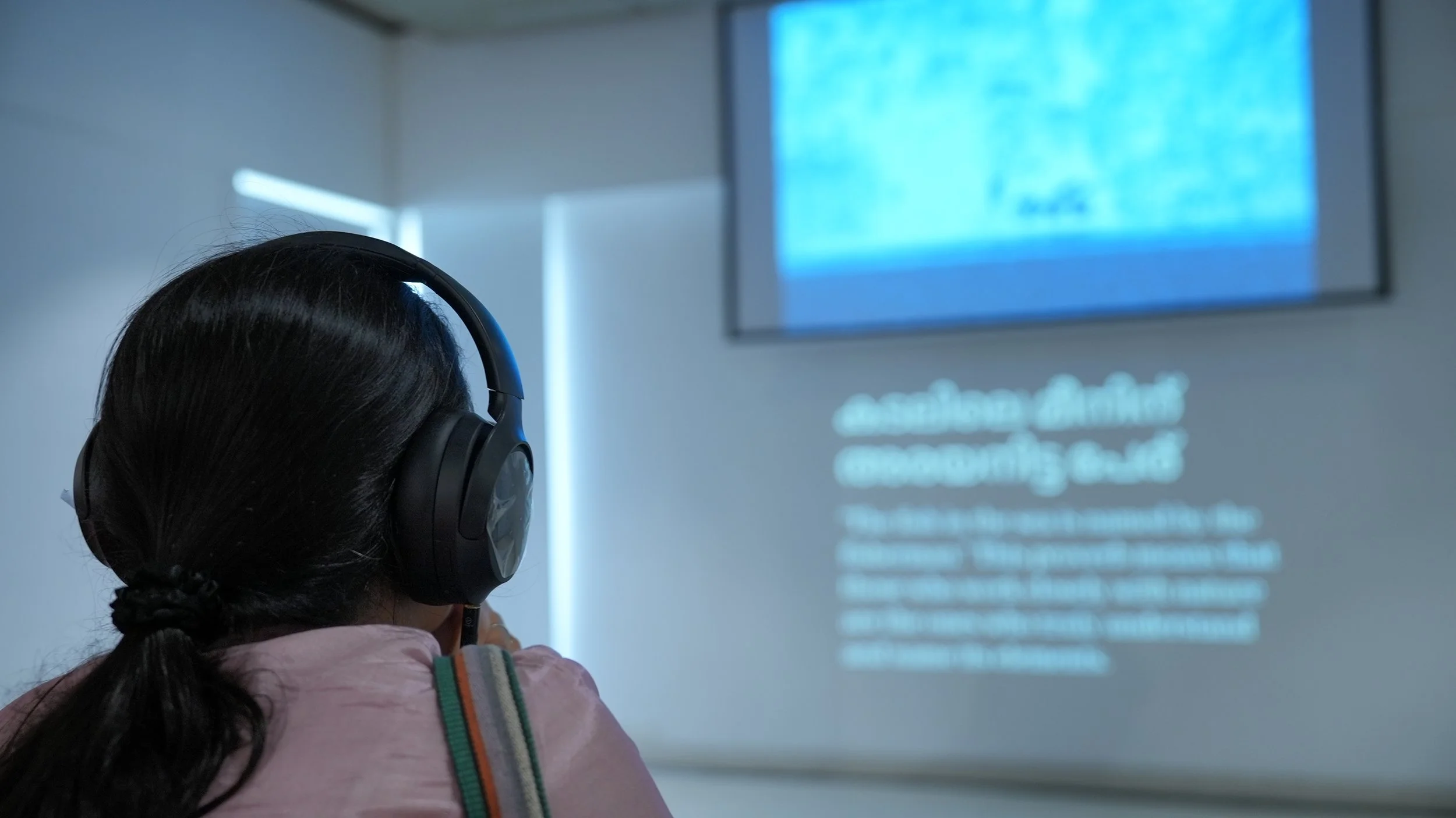 A visitor wearing headphones engages with the Words for Other Worlds installation by Lagori Collective, TDU, and Socratus Foundation, an immersive mixed media work exploring South Asian ecological language and climate knowledge.