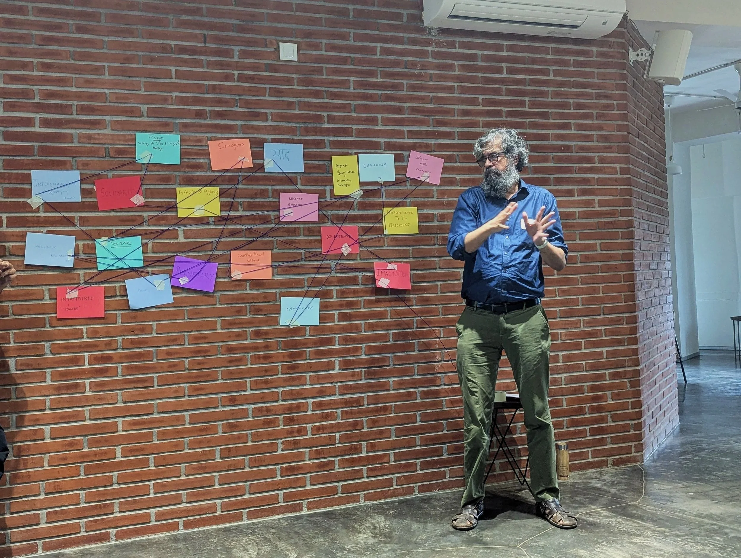 A practitioner presenting systems mapping with coloured sticky notes on a brick wall during the Weaving Co-Existence convening by Lagori Collective on multispecies coexistence in South Asia.