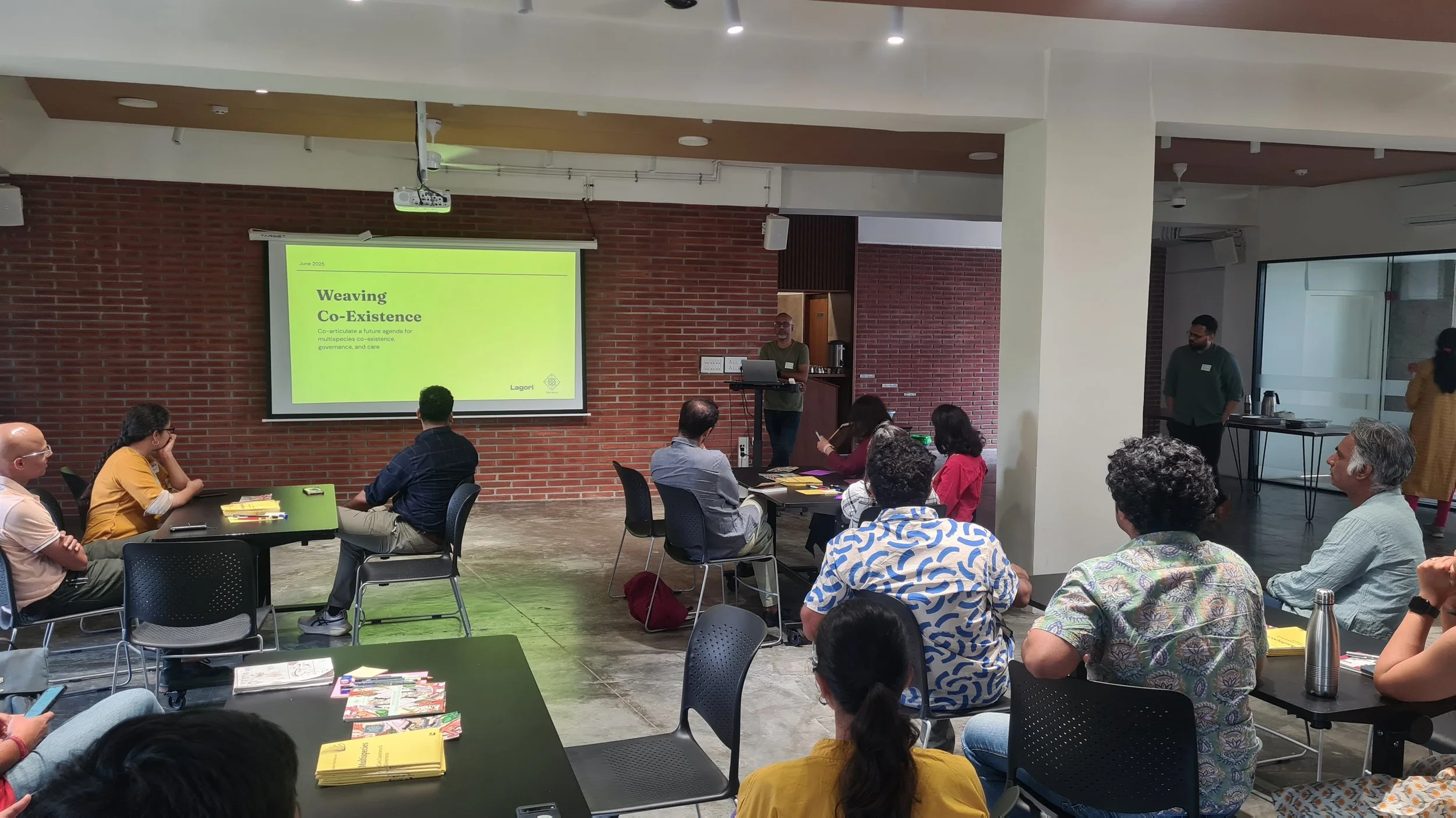 Opening plenary of the Weaving Co-Existence convening by Lagori Collective with the programme slide visible on screen and interdisciplinary practitioners seated in the audience.