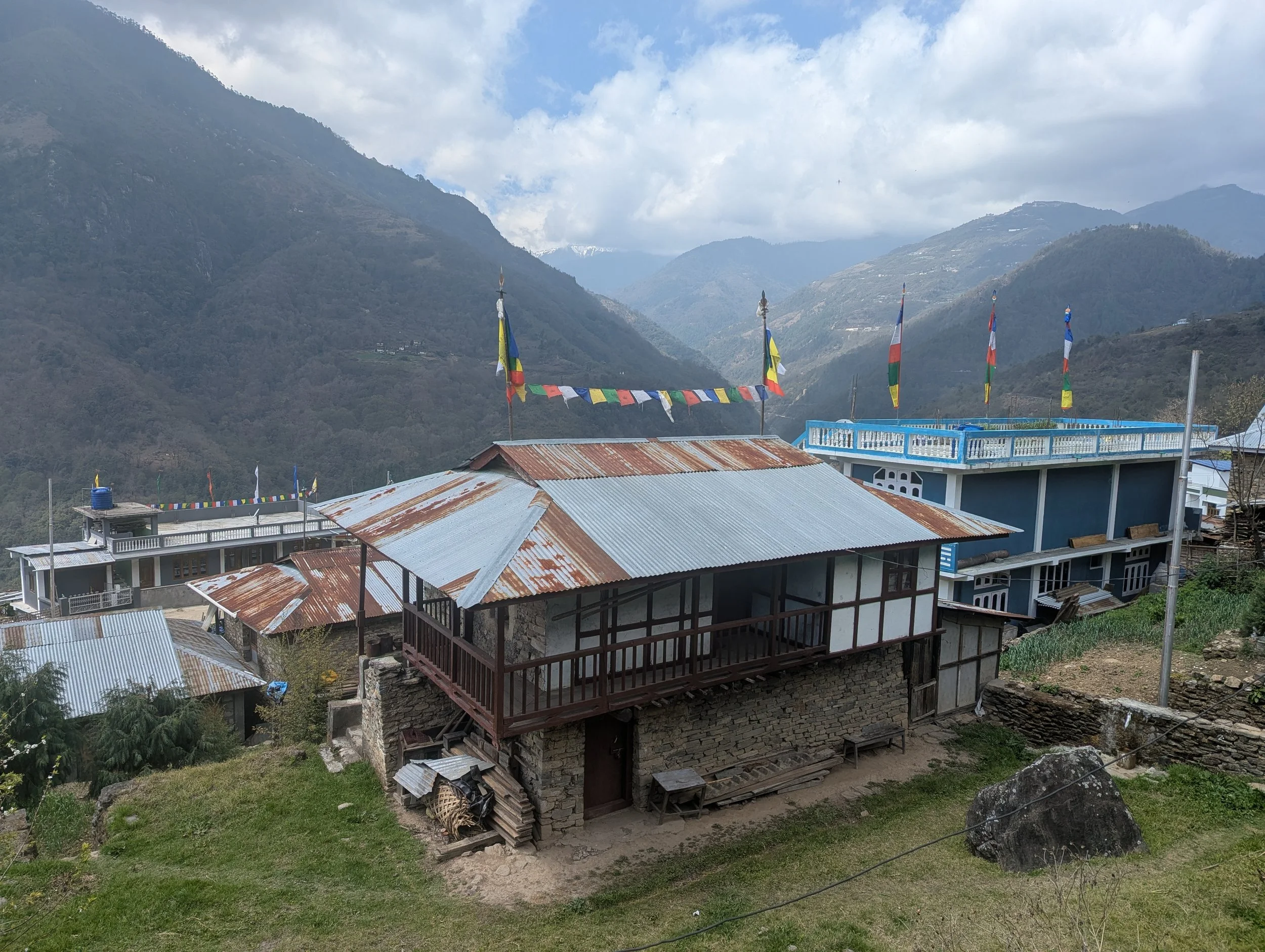 View of a Monpa village in Arunachal Pradesh with prayer flags and mountain ranges in the background, the field context for the Norbu Governance Futures project by Lagori Collective and It's All Folk.