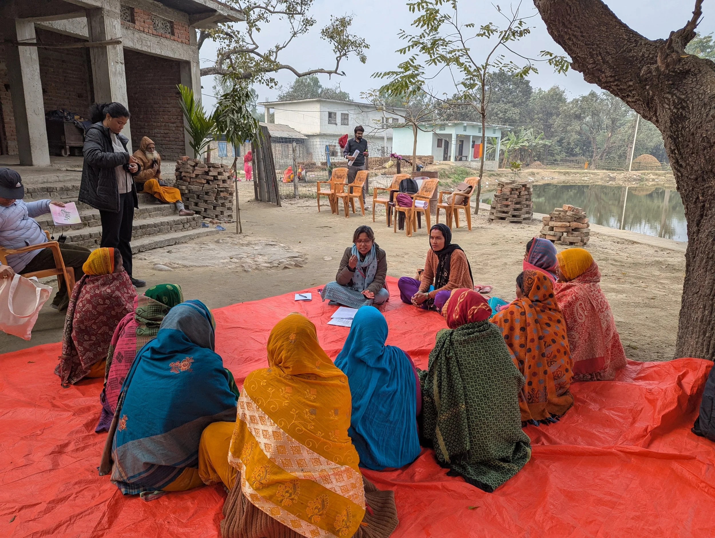 Participatory research session with women seated outdoors on a red mat in the Terai region of Nepal, during field research on gendered nutrition norms conducted by Lagori Collective with Helen Keller International and USAID.