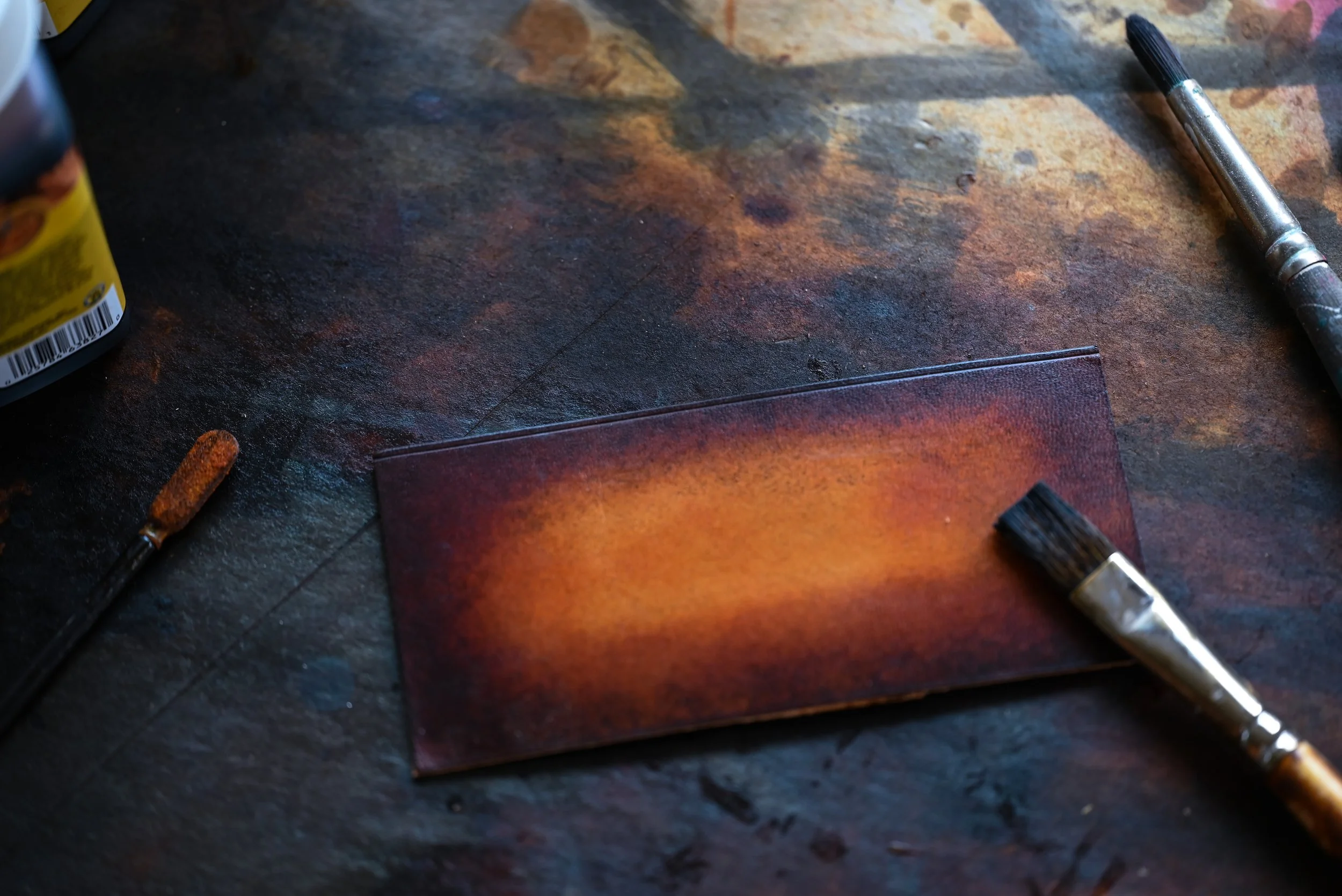 Un rectangle de cuir patiné posé sur une surface de travail pleine de taches de teinture