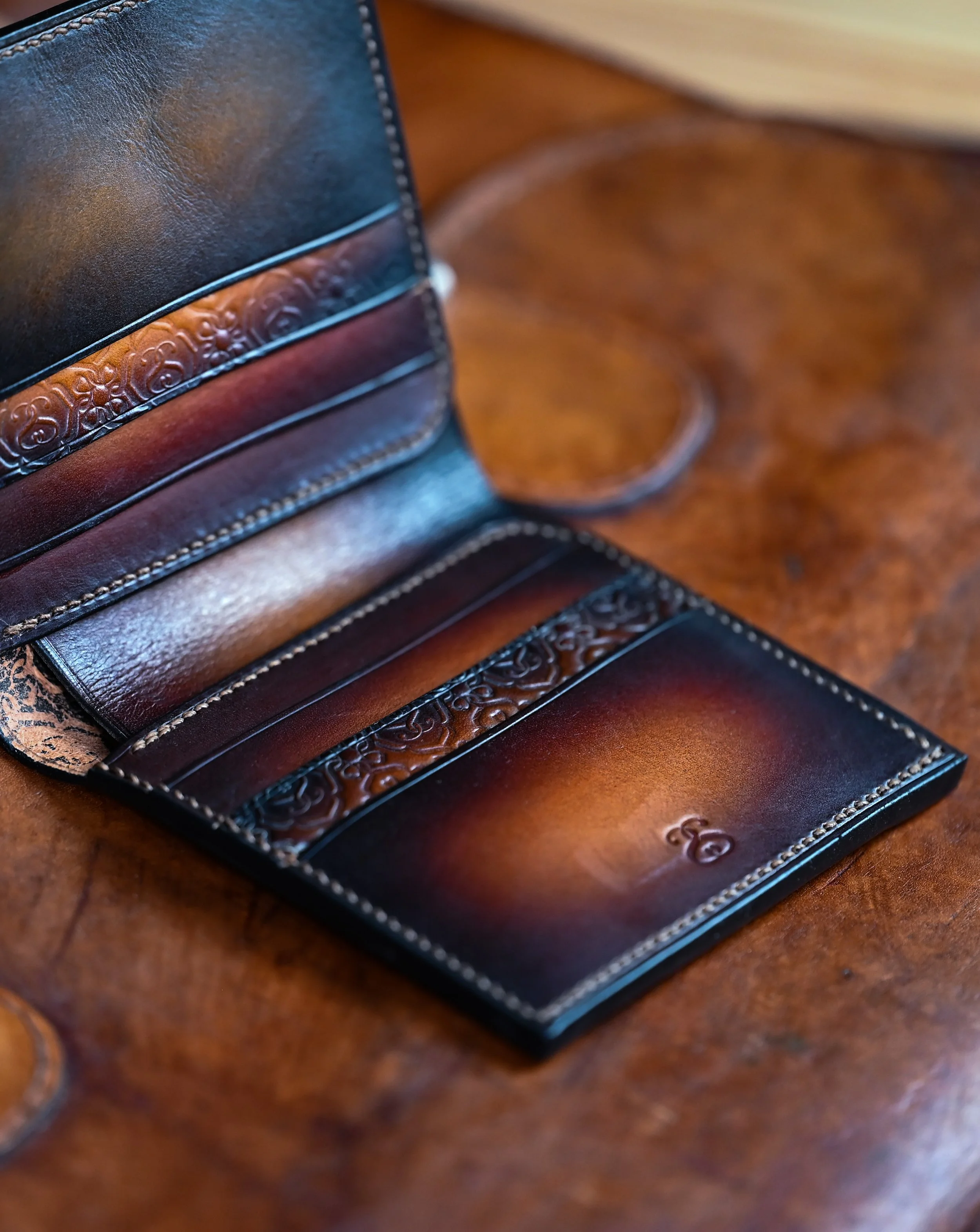 Portefeuille en cuir tanné végétal et patiné, avec des motifs embossés ouvert sur une table en bois.
