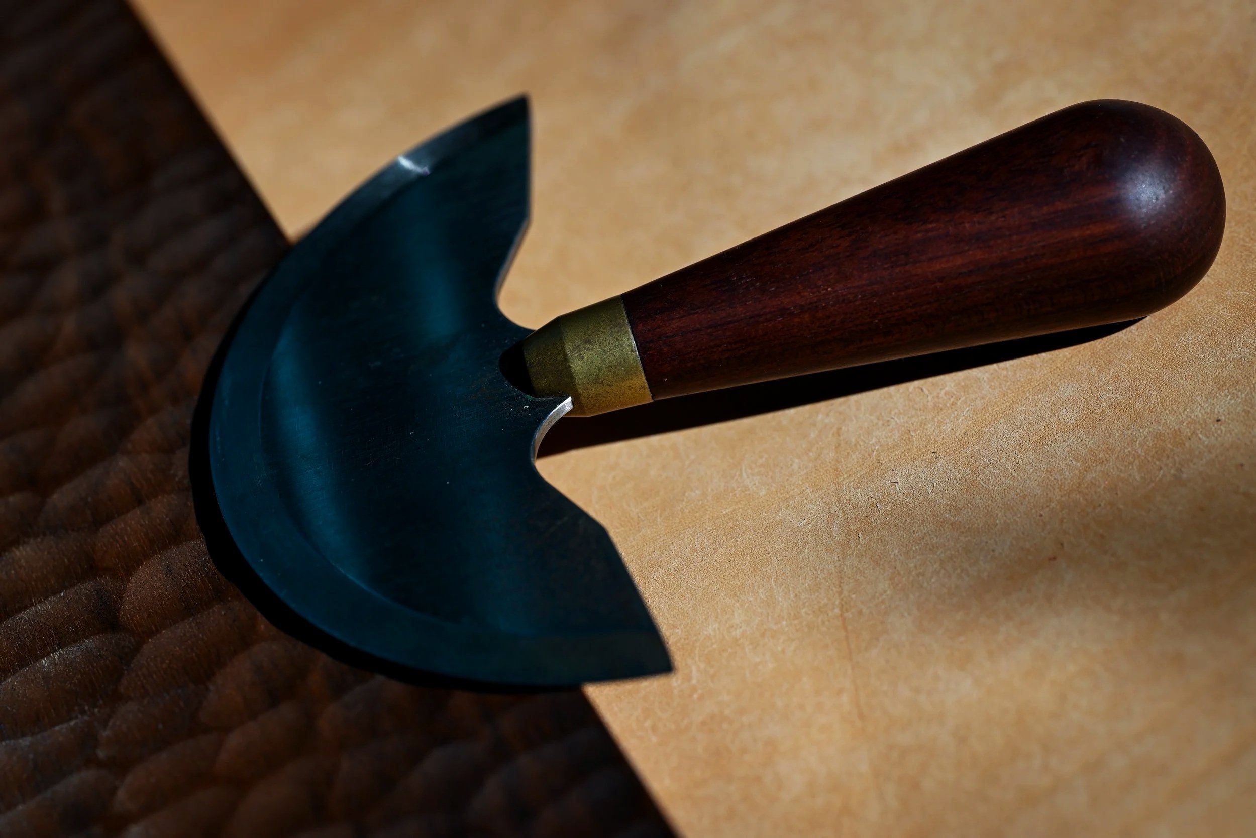 Un couteau demi-lune de maroquinier posé sur un morceau de cuir tanné végétal