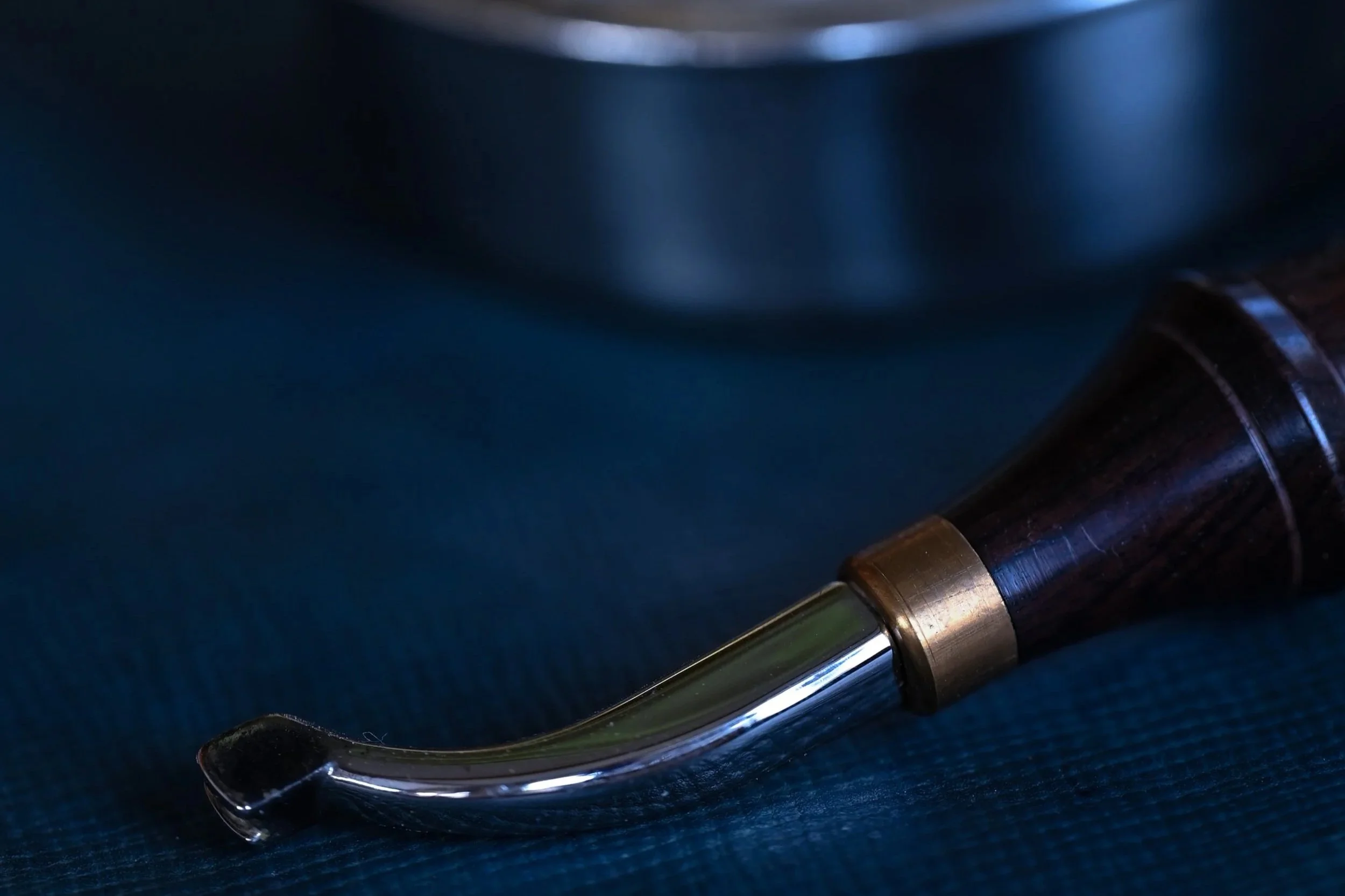Flet de maroquinier métalique et au manche en bois posé sur un morceau de cuir couleur indigo
