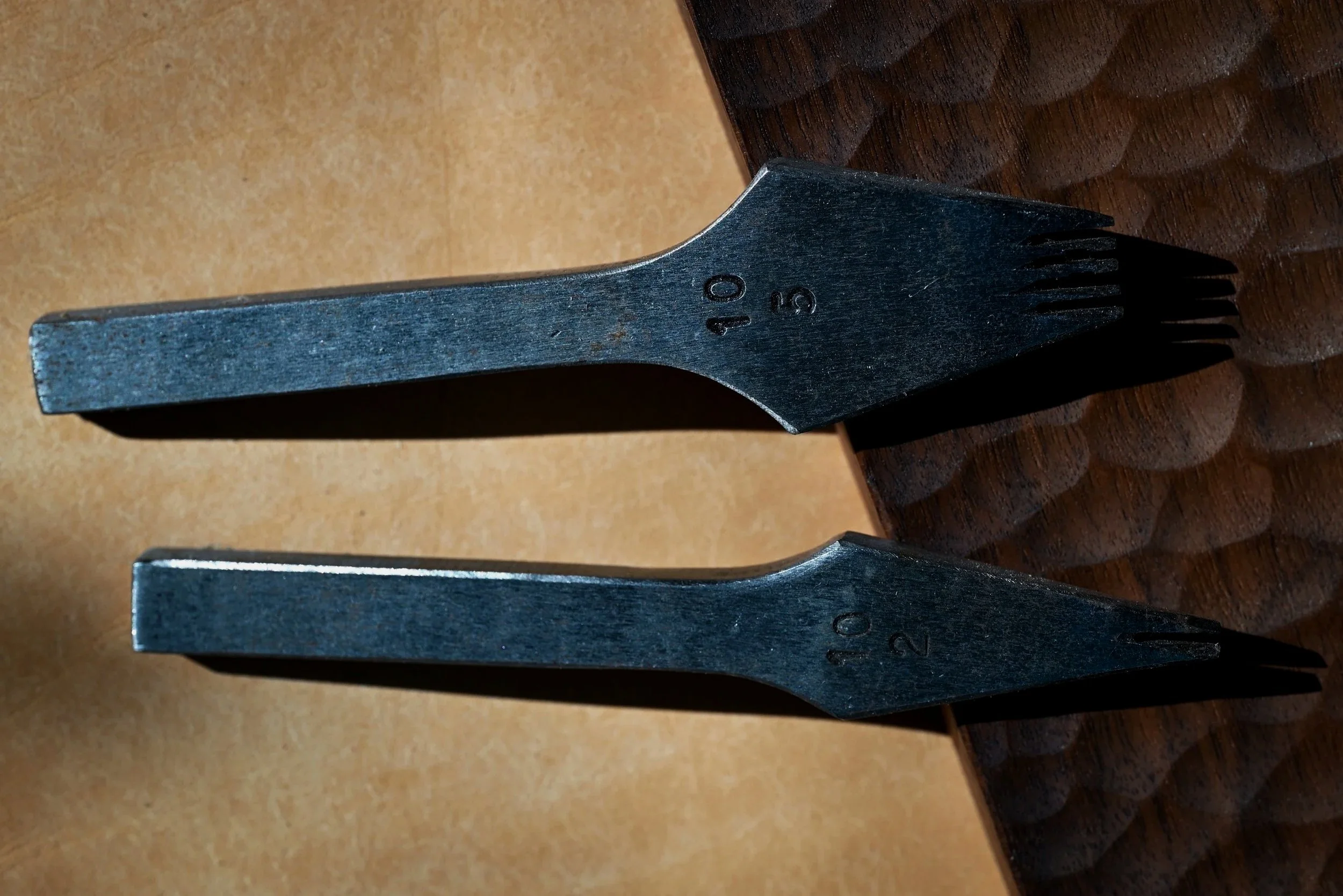 Une paire de griffes à frapper de maroquinier posées sur un morceau de cuir et un table en bois ancien