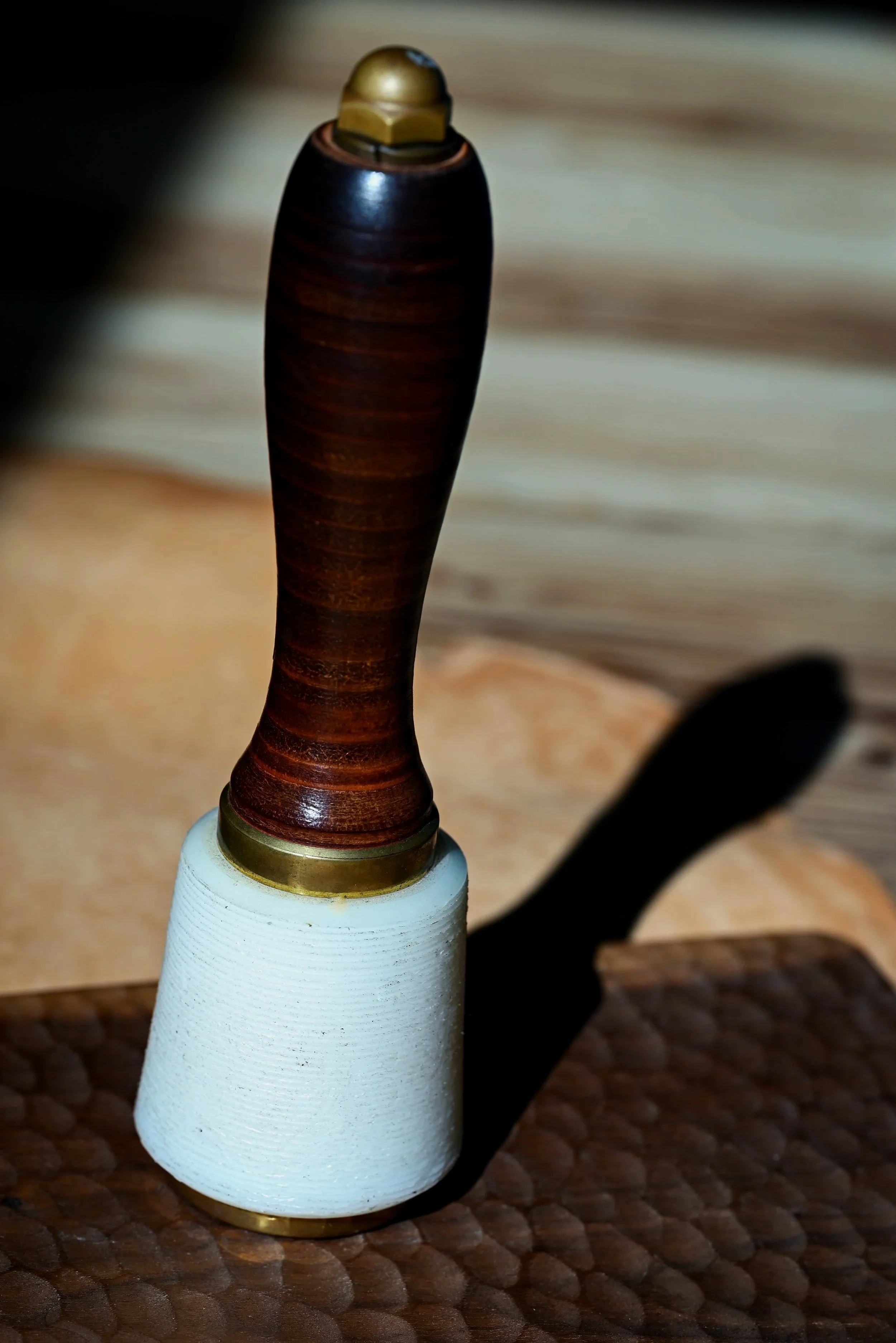 Un maillet au manche en bois et à la tête en plastique blanc posé sur une surface en bois ancien