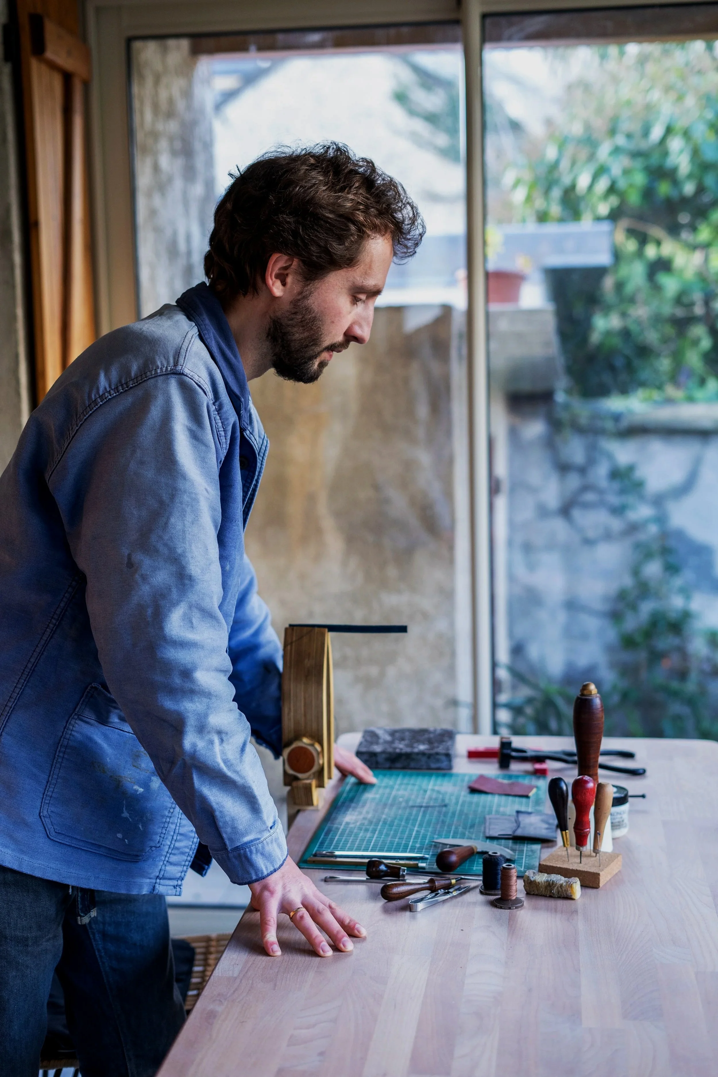 Homme avec une veste de travail bleu devant une table avec divers outils de maroquinier